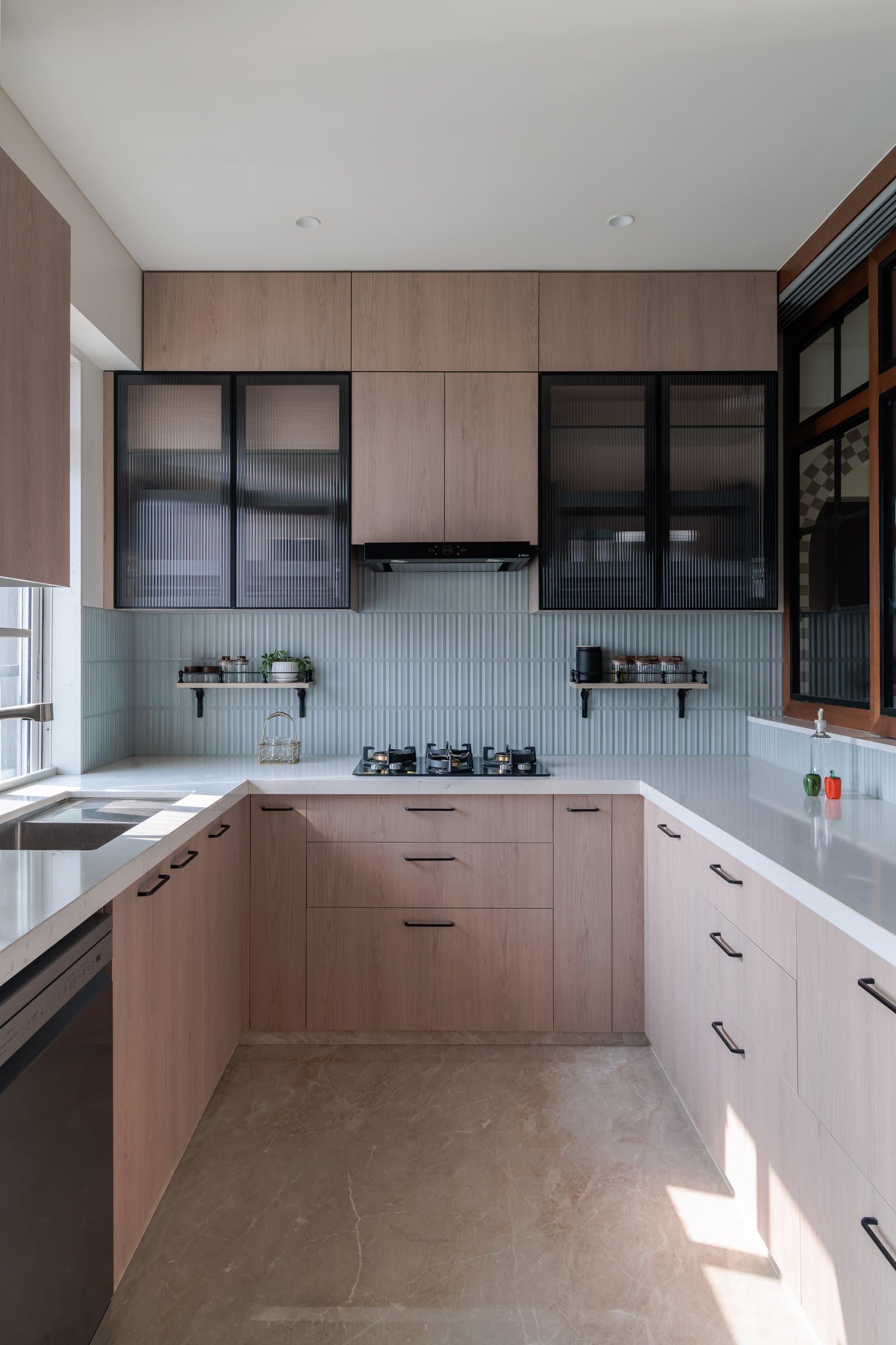 The kitchen steps into a cleaner register: light oak, ribbed tile, and fluted glass in black frames