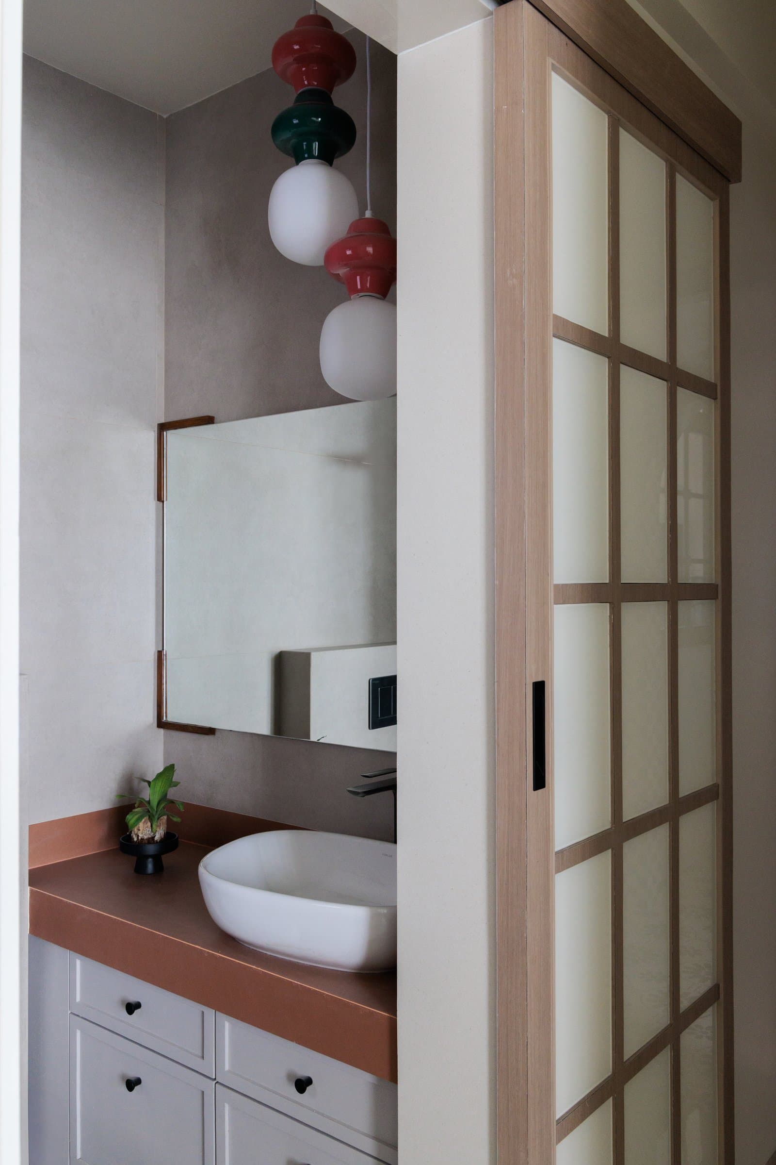 A bathroom with a terracotta counter and colourful stacked-sphere pendant lights, a small confident gesture of playfulness