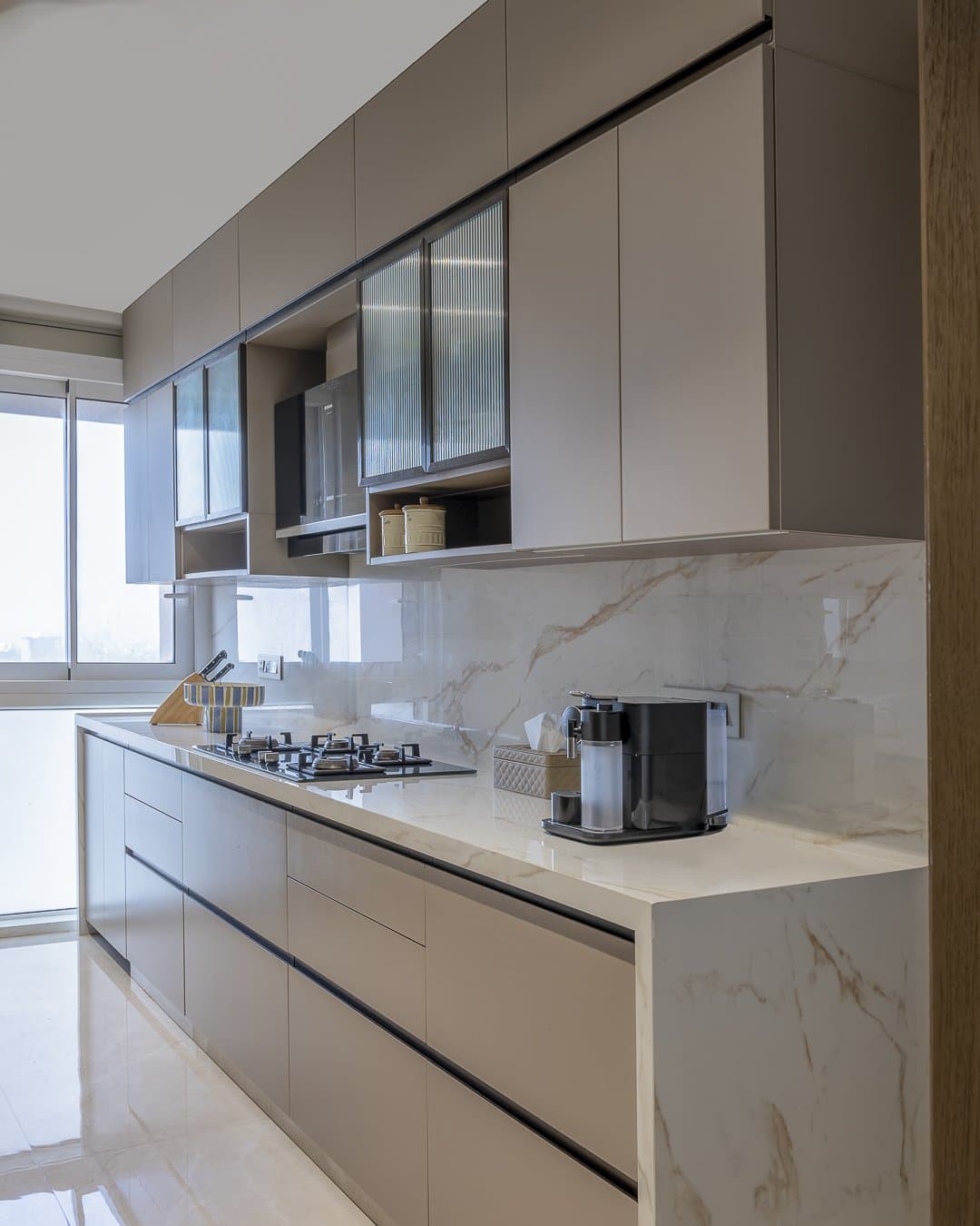 The kitchen maintains the home's neutral discipline through pale cabinetry and veined stone