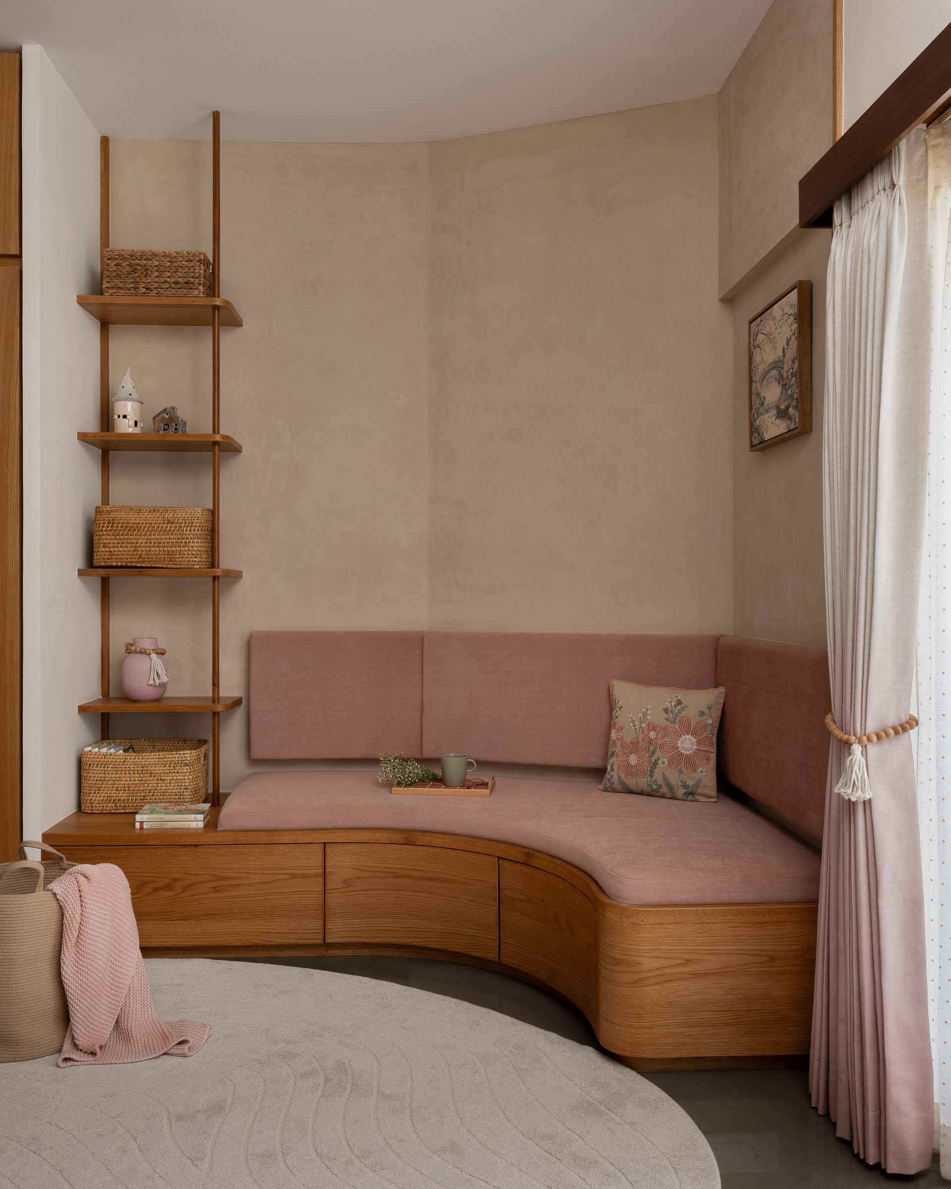 The children's bay seat: a curved, storage-integrated window seat in dusty rose velvet that softens the room's geometry without announcing the fact