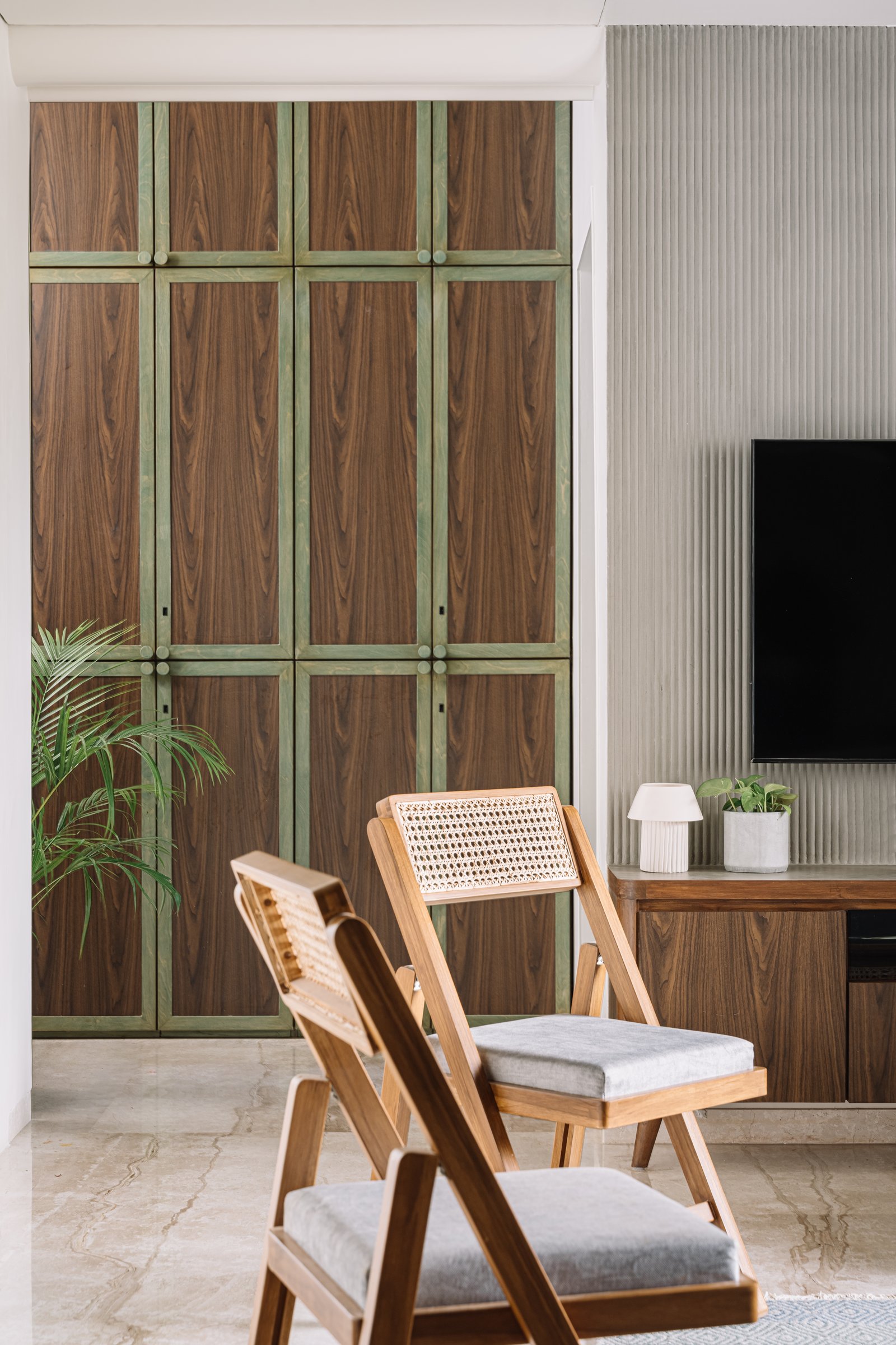The entrance passage: walnut cabinetry with oxidised green framing establishes the home's craft palette alongside the fluted TV wall