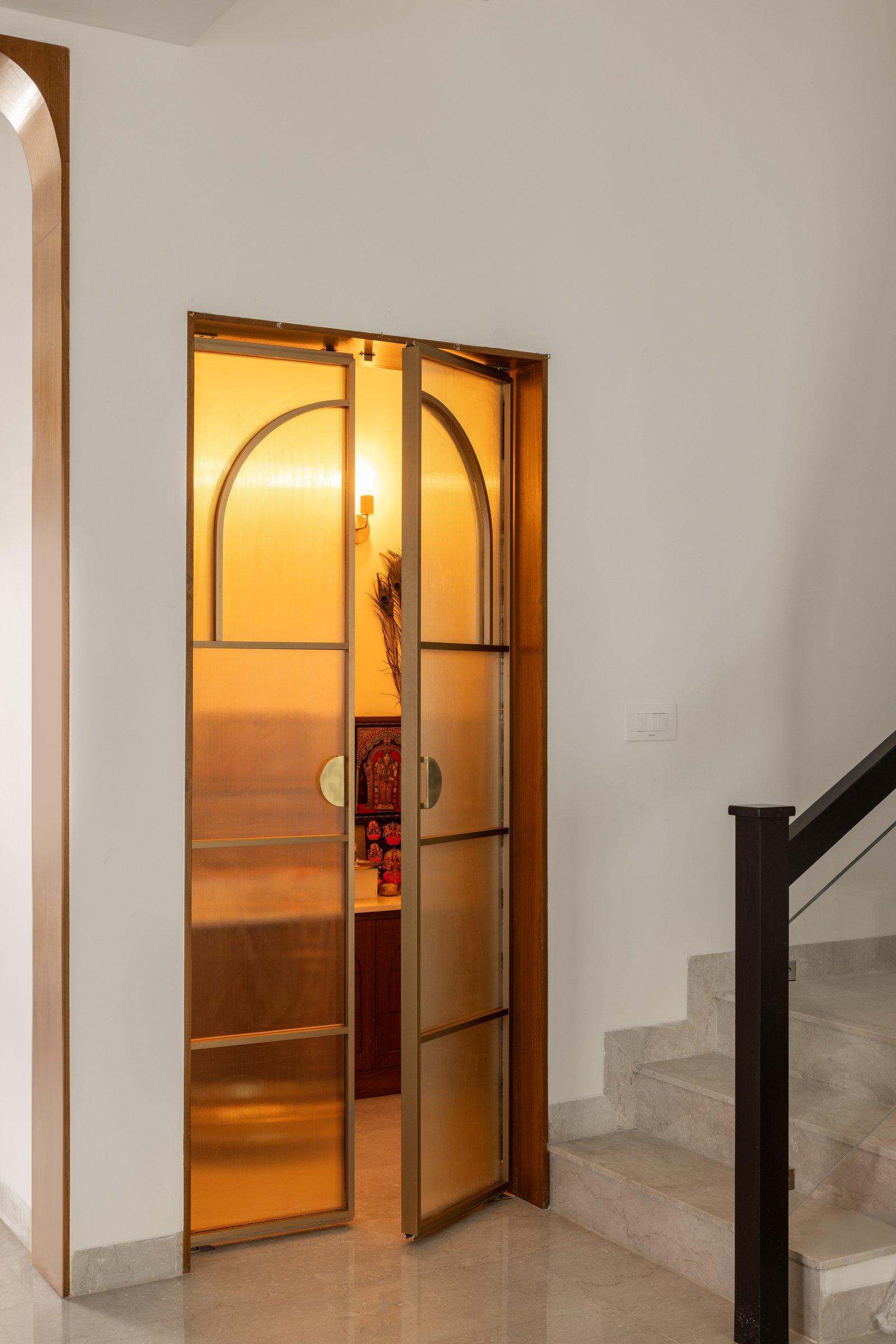 The pooja room, enclosed by arched amber glass-and-metal doors that filter light with quiet reverence