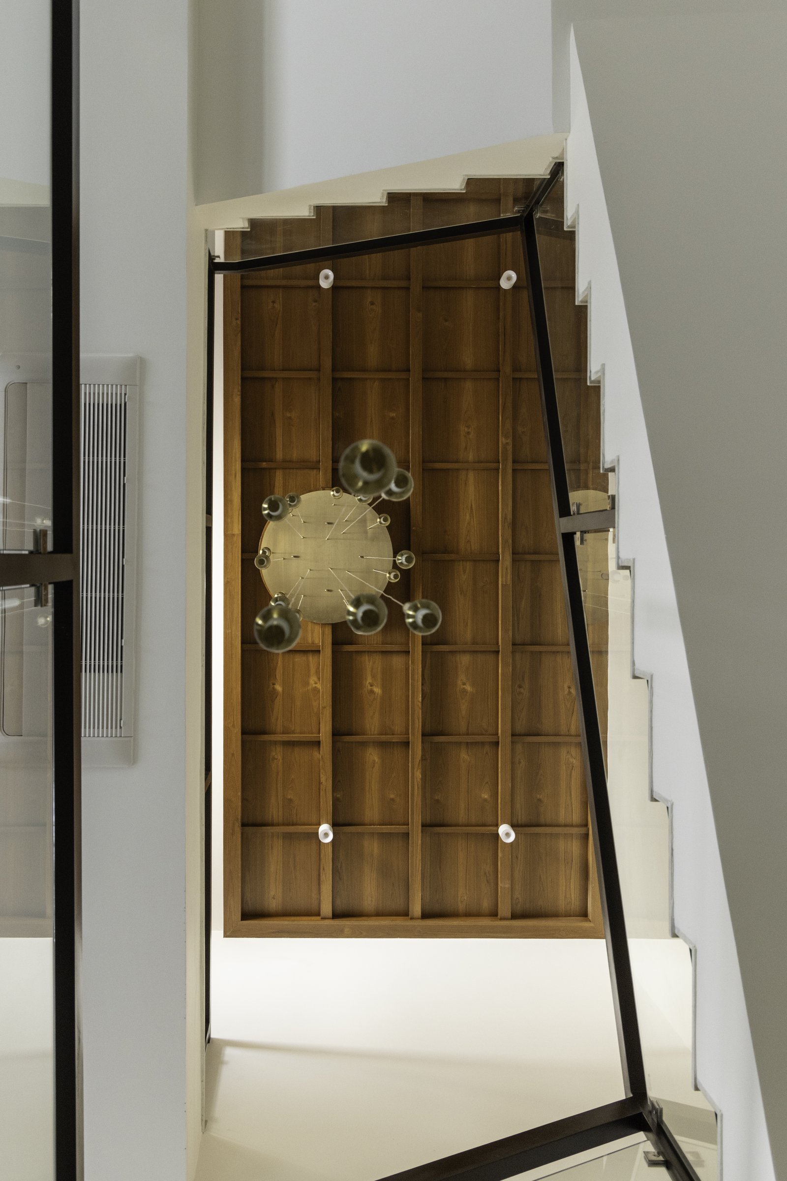 The staircase ceiling, transformed by a veneer grid and suspended brass chandelier into a spatial event