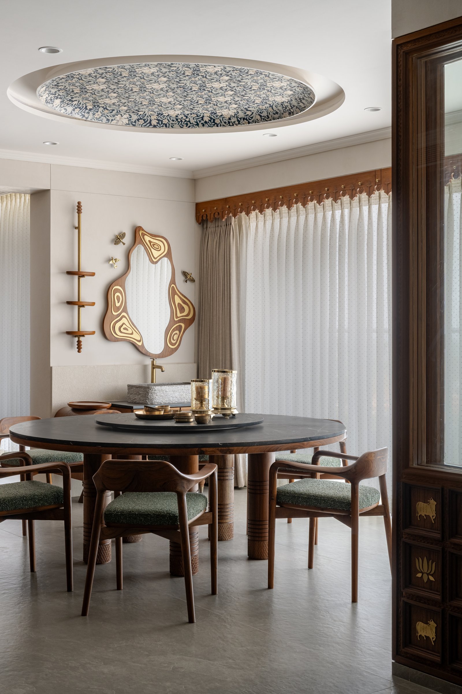 Wing A's dining area beneath a recessed floral ceiling medallion, the glass-walled pooja room visible beyond
