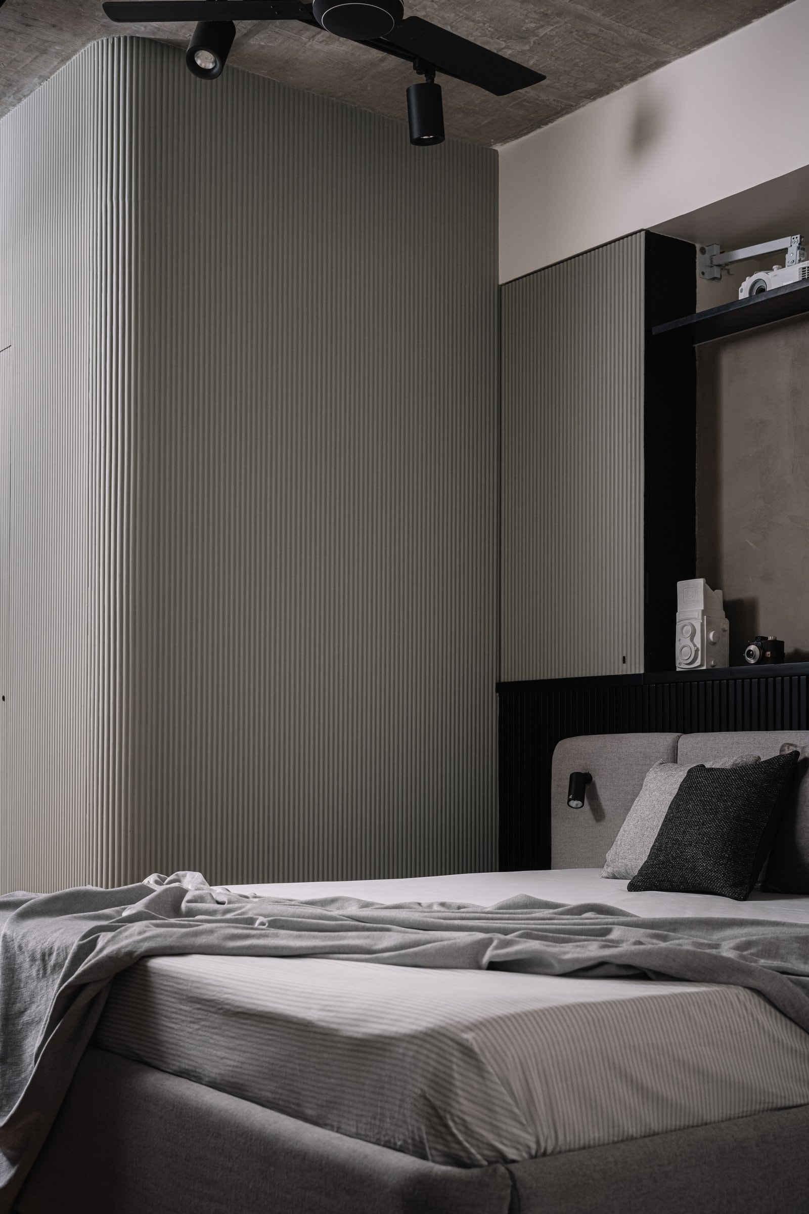 The master bedroom in grey-green fluted panels and exposed concrete, a deliberate shift to restraint