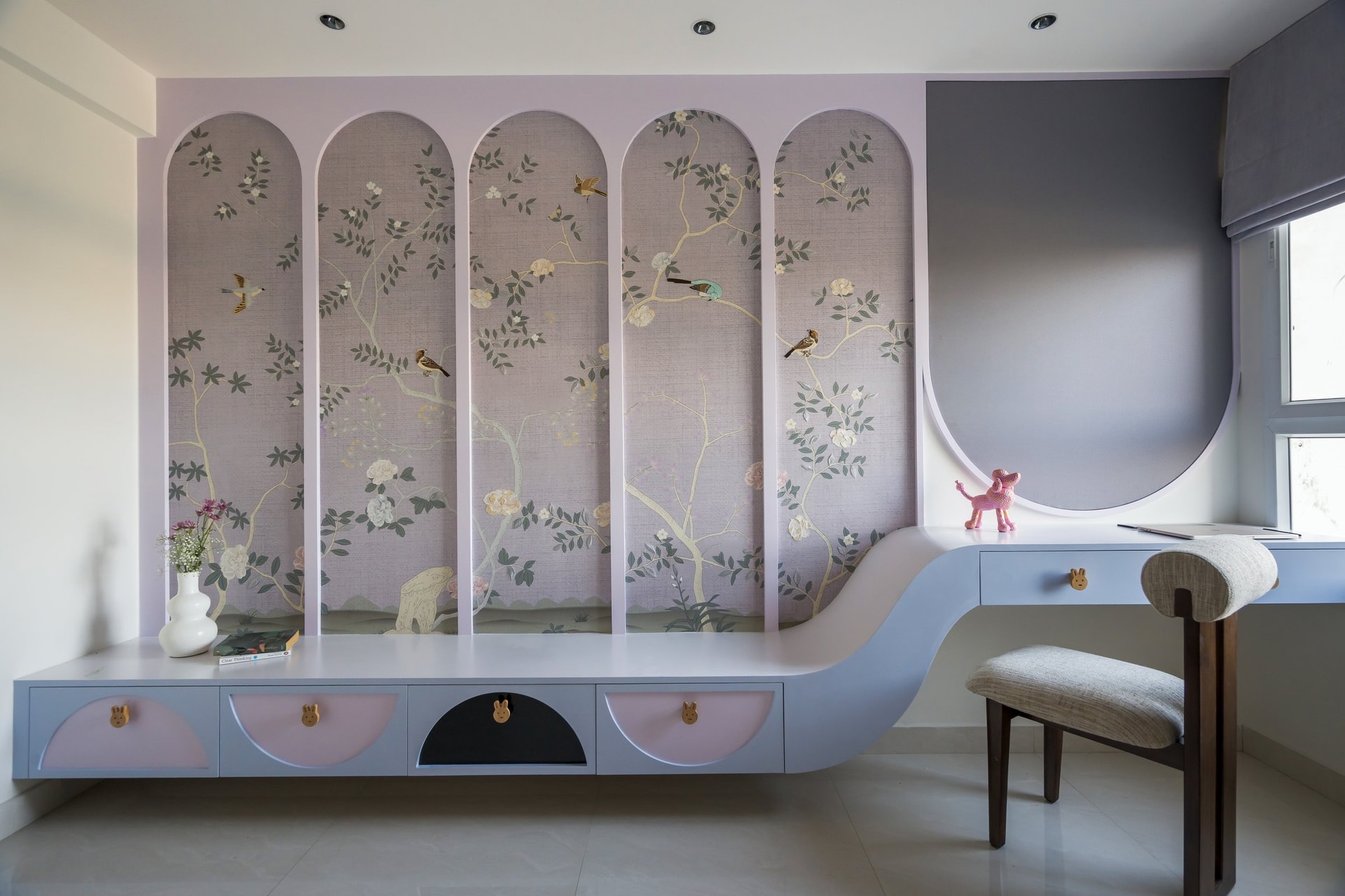 The child's room, where arched wallpaper panels and a wave-form storage unit shift the palette to lavender and pale blue