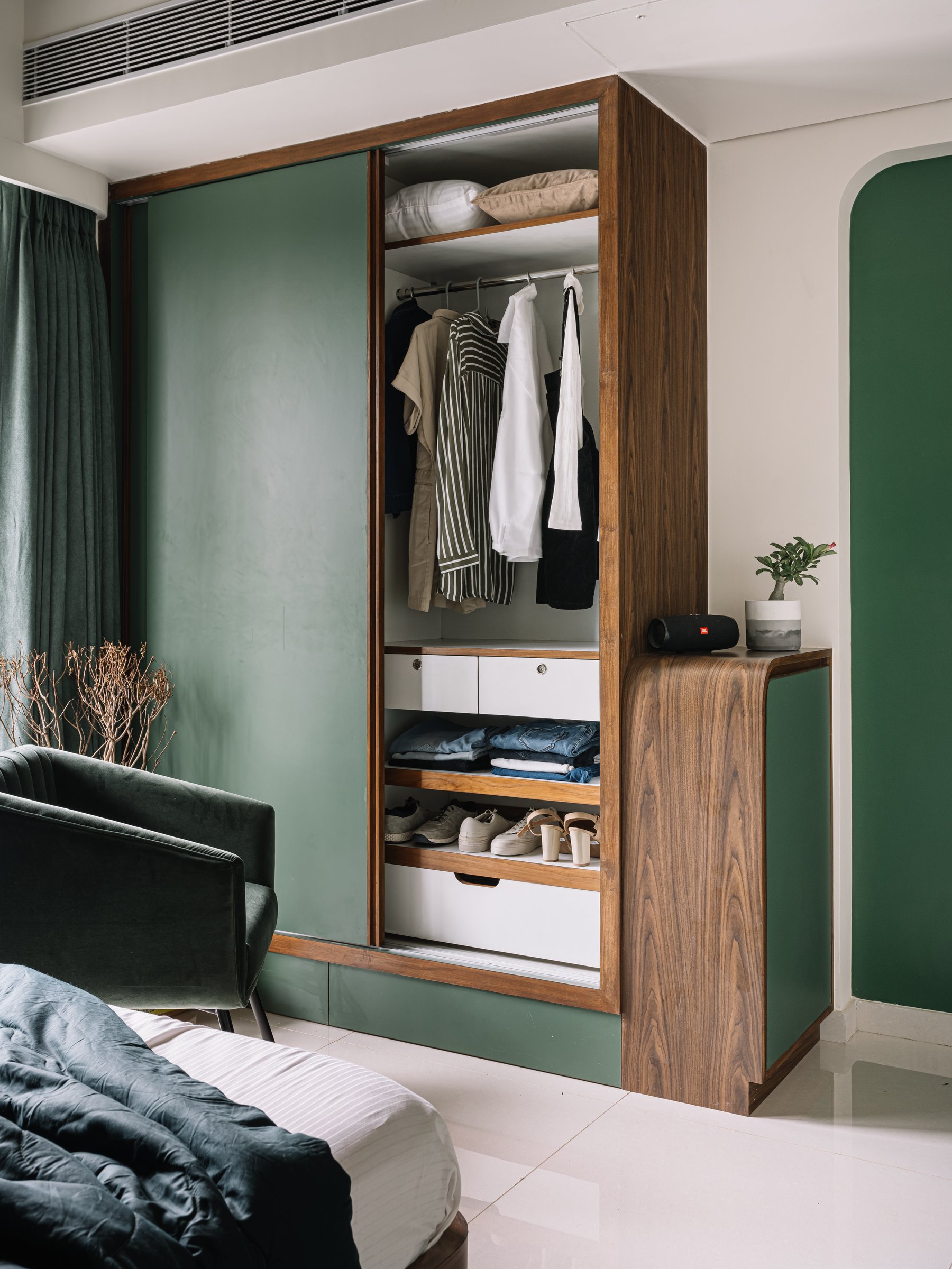 The daughter's wardrobe: green sliding doors in walnut framing, the curved console stepping down beside it