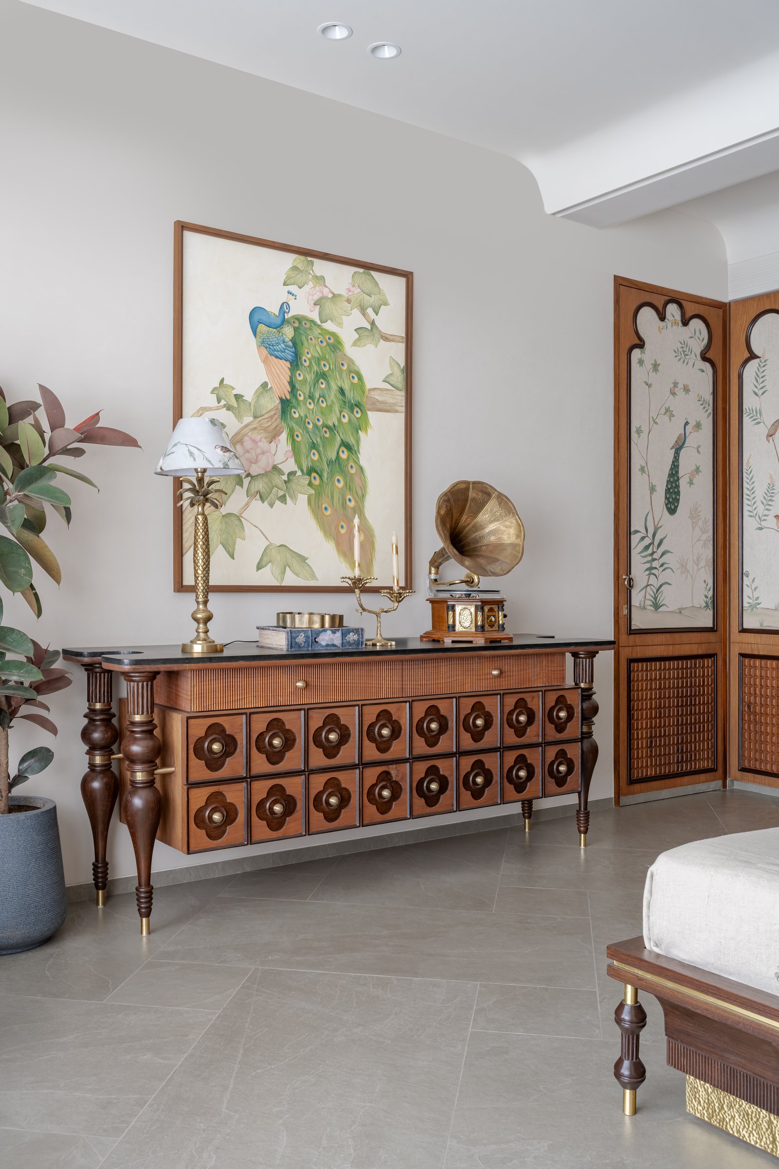 A custom console with flower-motif drawer pulls below a peacock painting, with chinoiserie screen panels to the dressing area