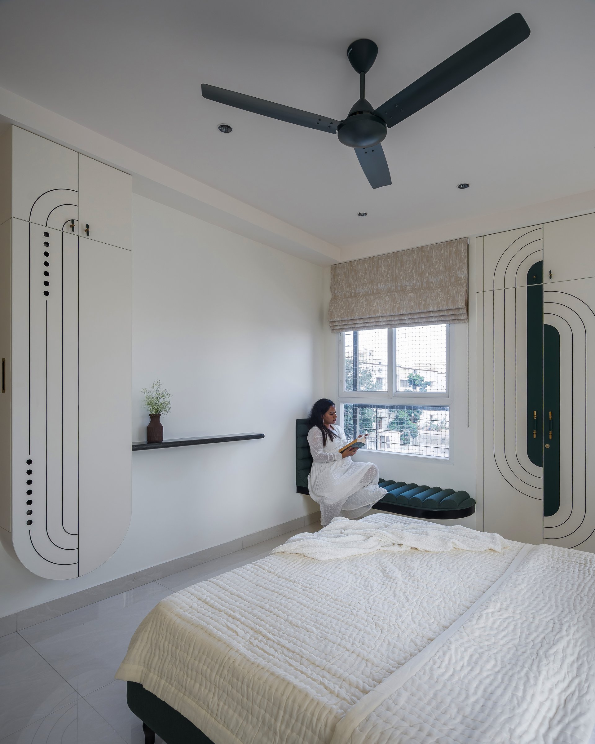 The second bedroom seen from the foot of the bed, with a built-in window seat and flanking storage walls framing a reading nook