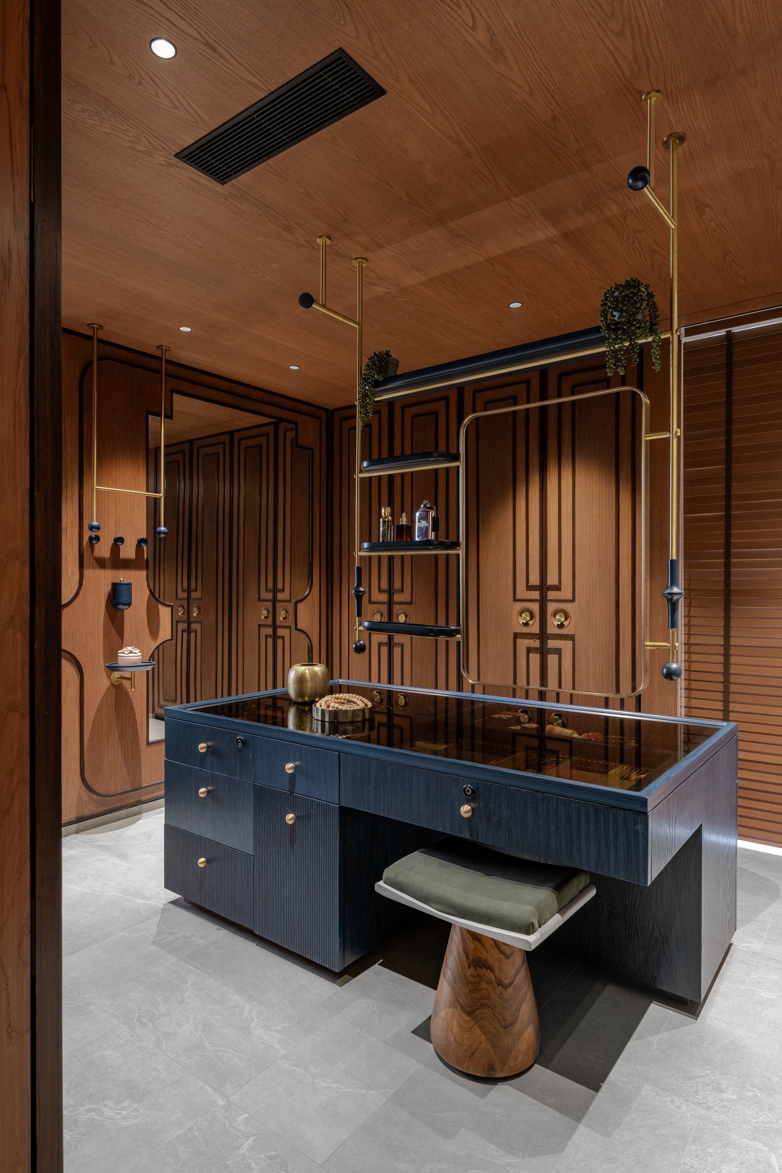 The master dressing room as jewellery atelier: panelled walls in timber and navy lacquer around a glass-topped island vanity