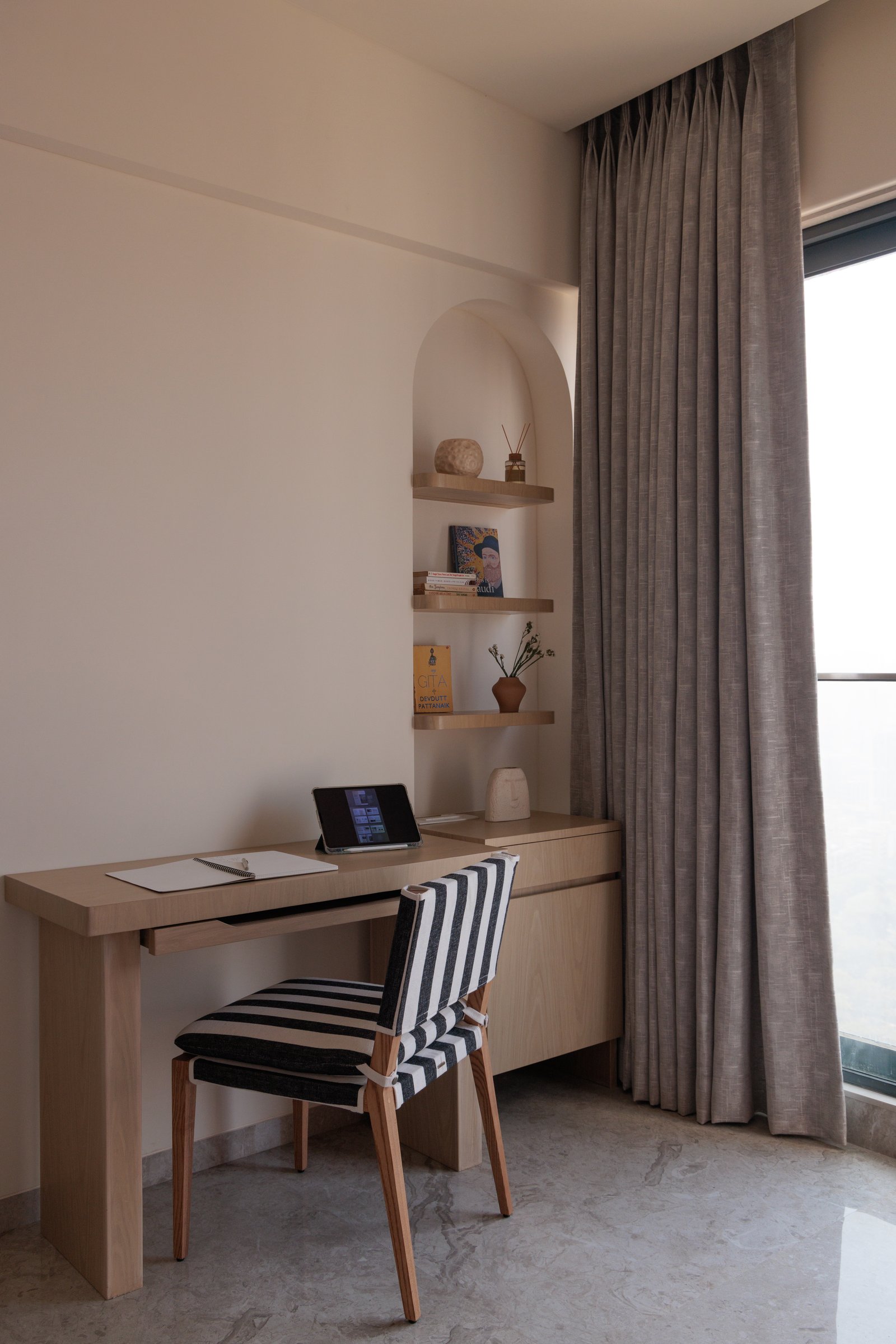The den workspace, with a timber desk beneath an arched niche and the home's recurring striped upholstery