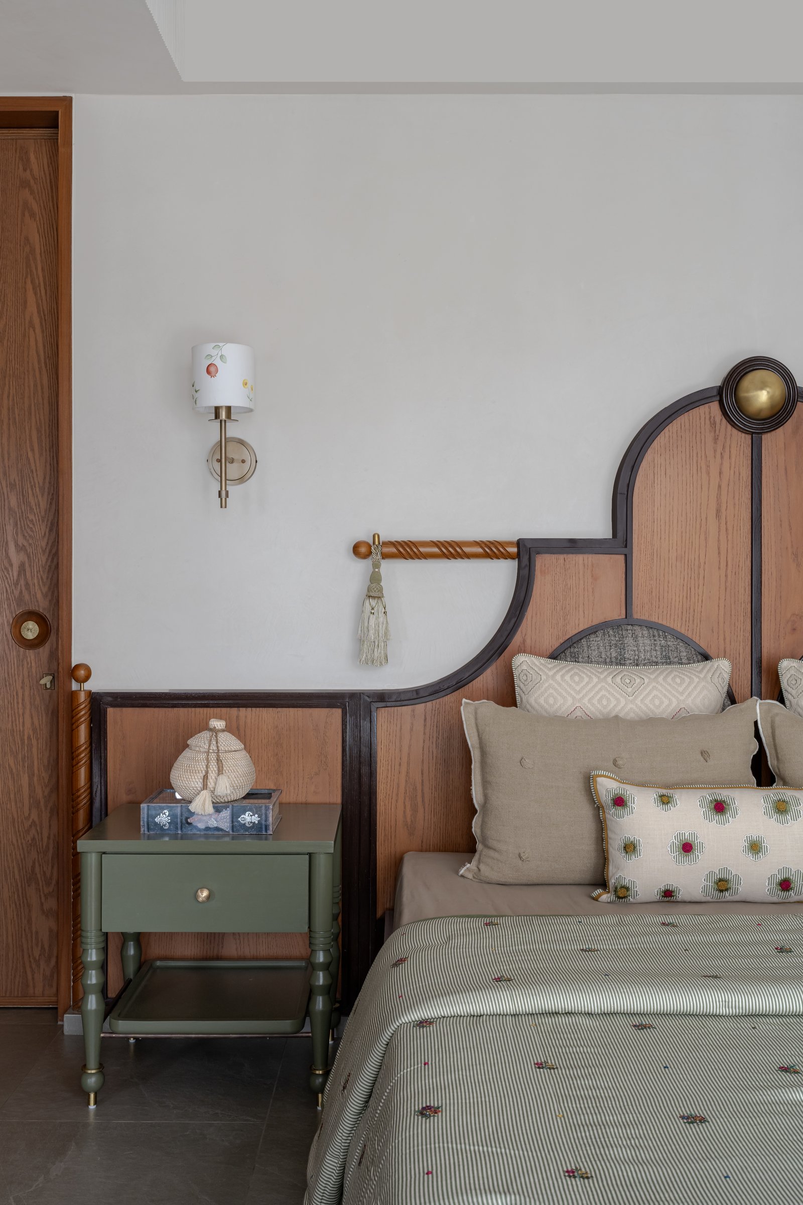 The arched headboard with brass finial and olive-green bedside tables in the daughter's room