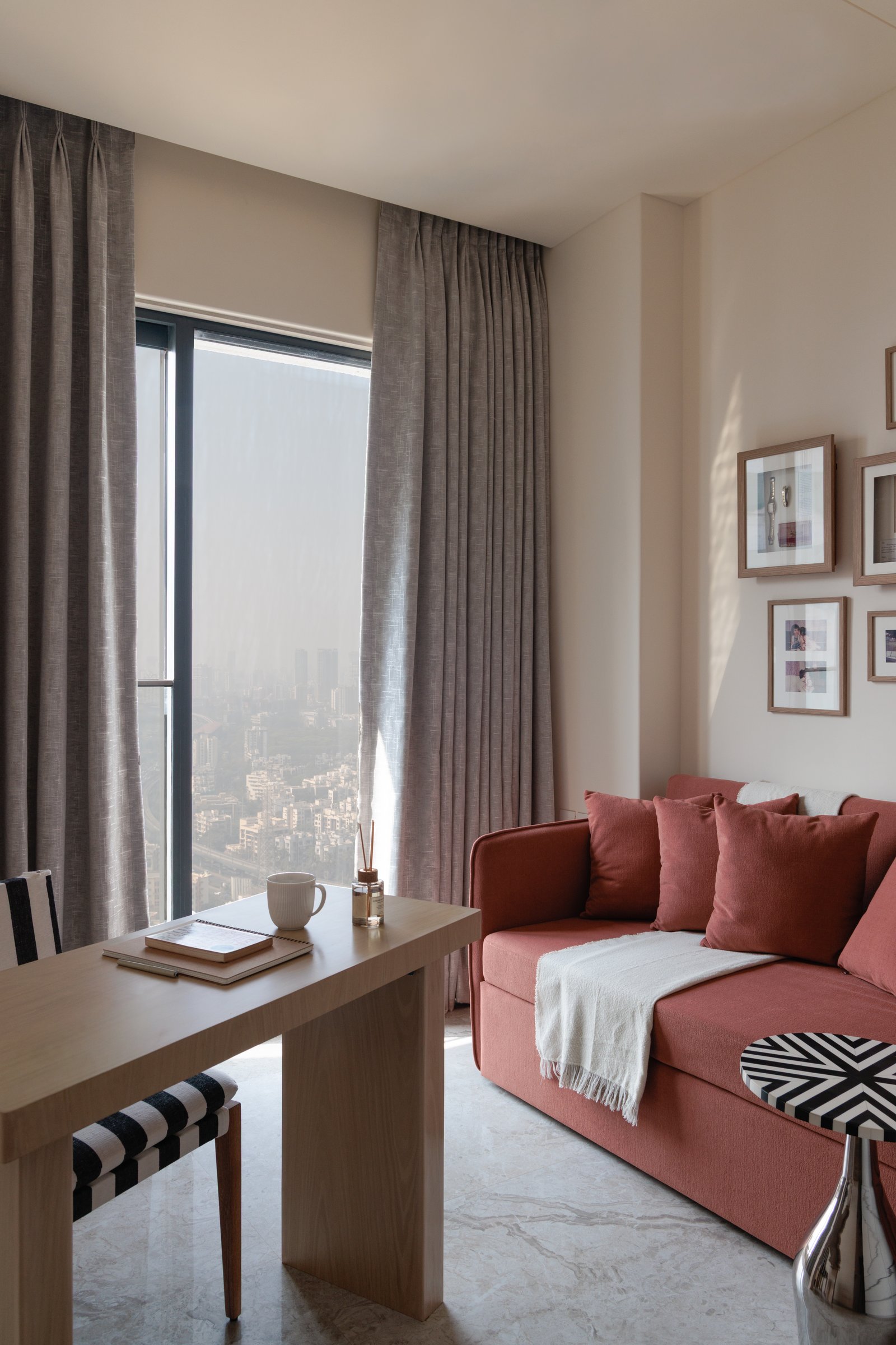 The den's terracotta sofa and city view, the one moment where colour breaks free of the apartment's muted register