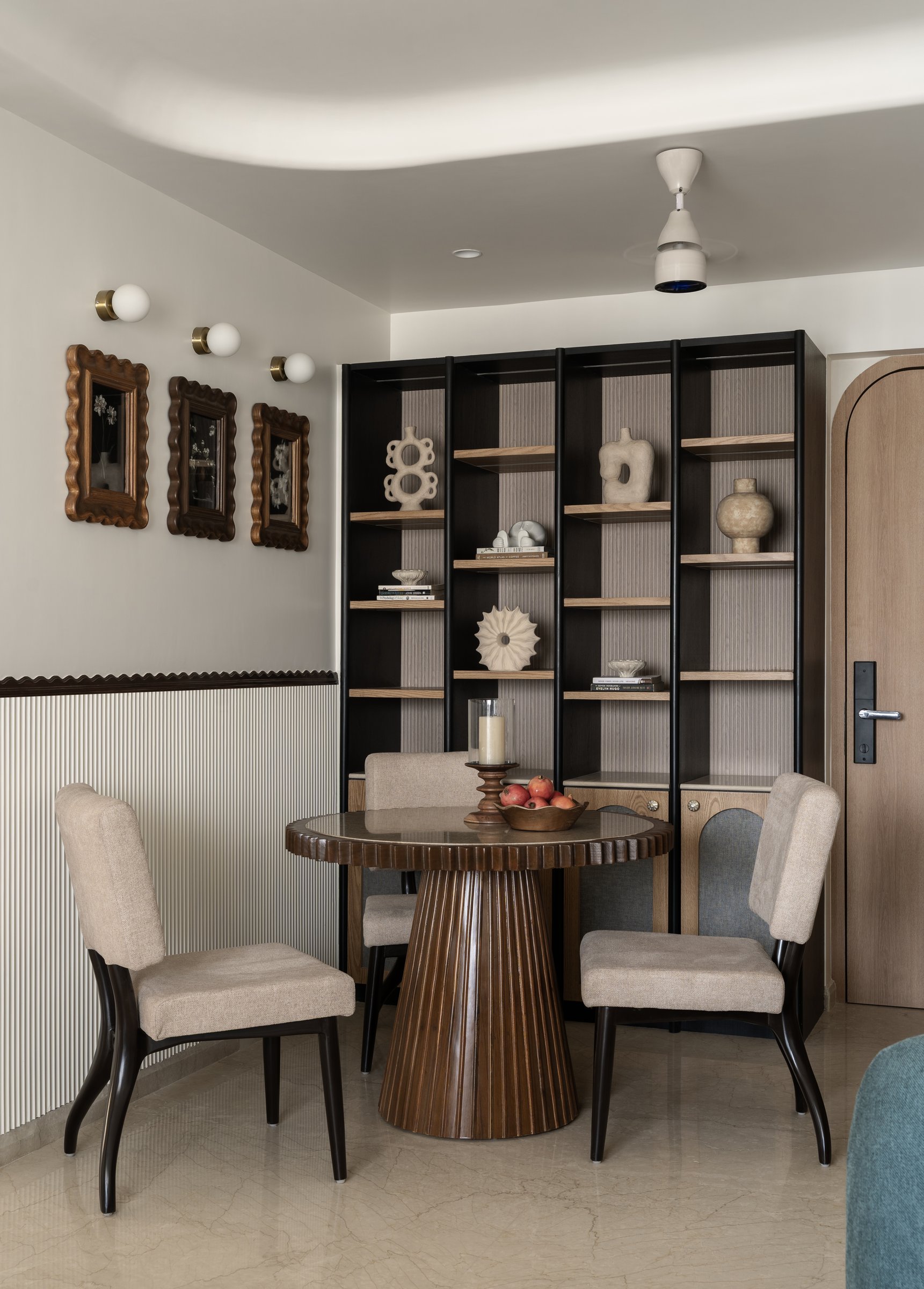 The dining alcove, anchored by a fluted wood pedestal table and a tall reeded display unit