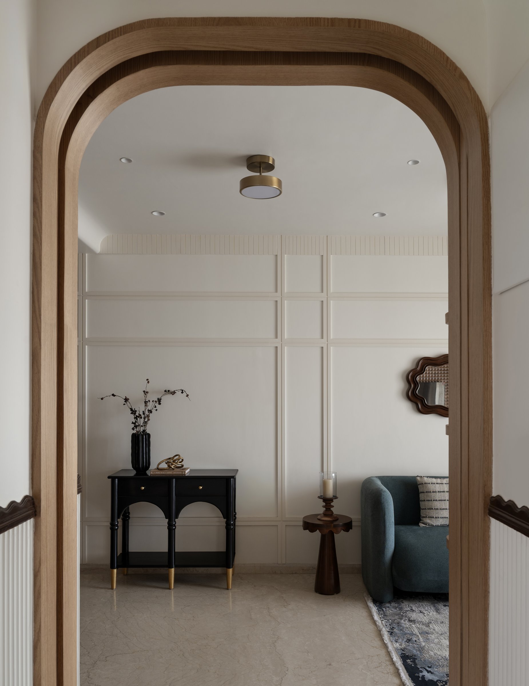 The arched timber portal frames the foyer, where a black turned-leg console establishes the home's vocabulary of curve and quiet ornament