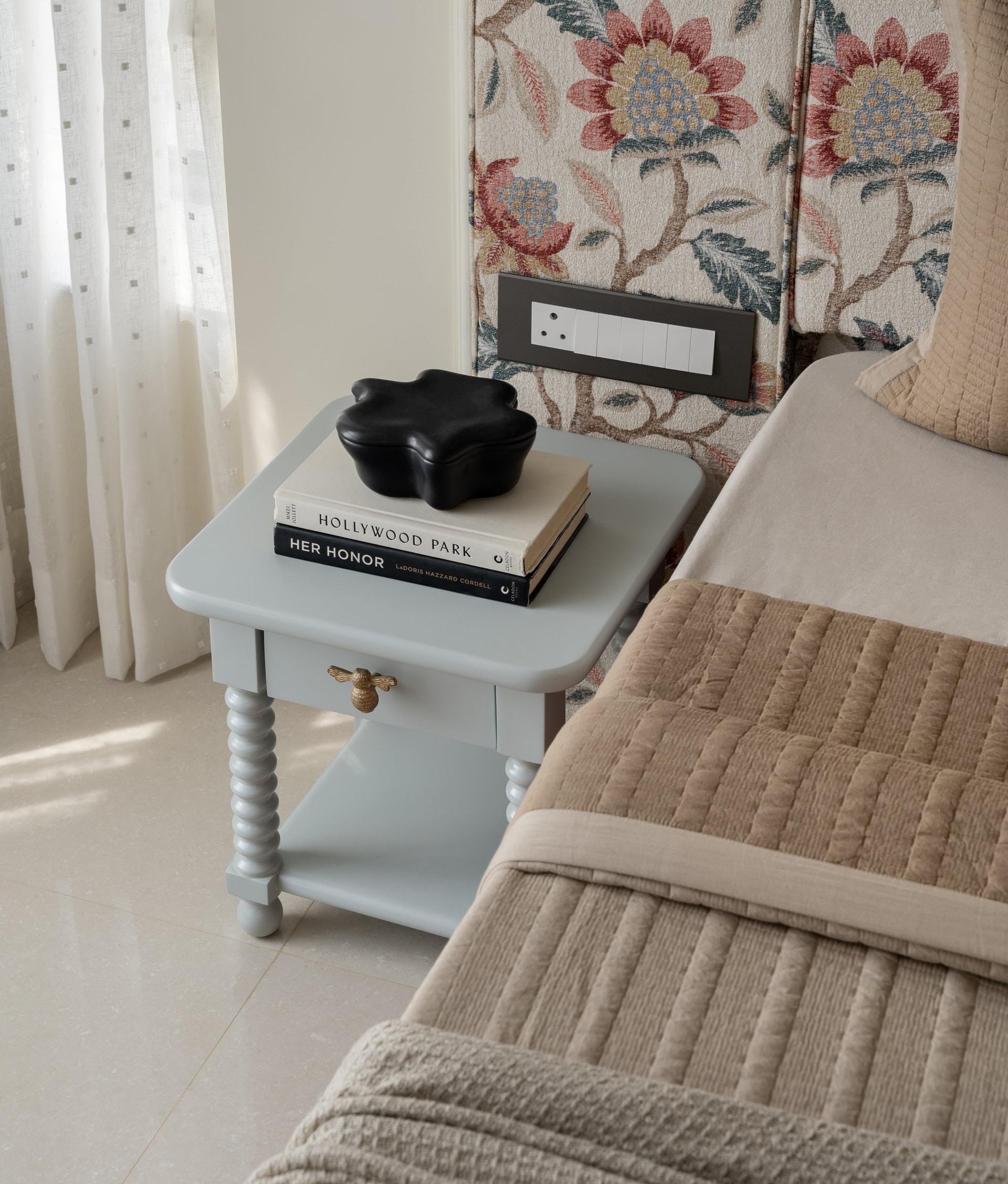 A dove-blue bedside table with bobbin-turned legs and a single brass bee-shaped pull