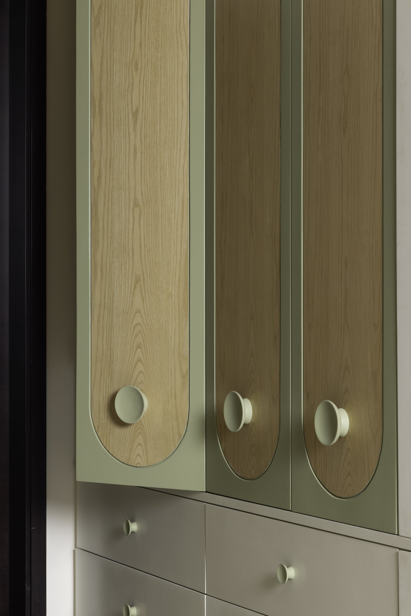 Wardrobe detail in the daughter's room, where oak panels meet sage-green finishes with rounded handles