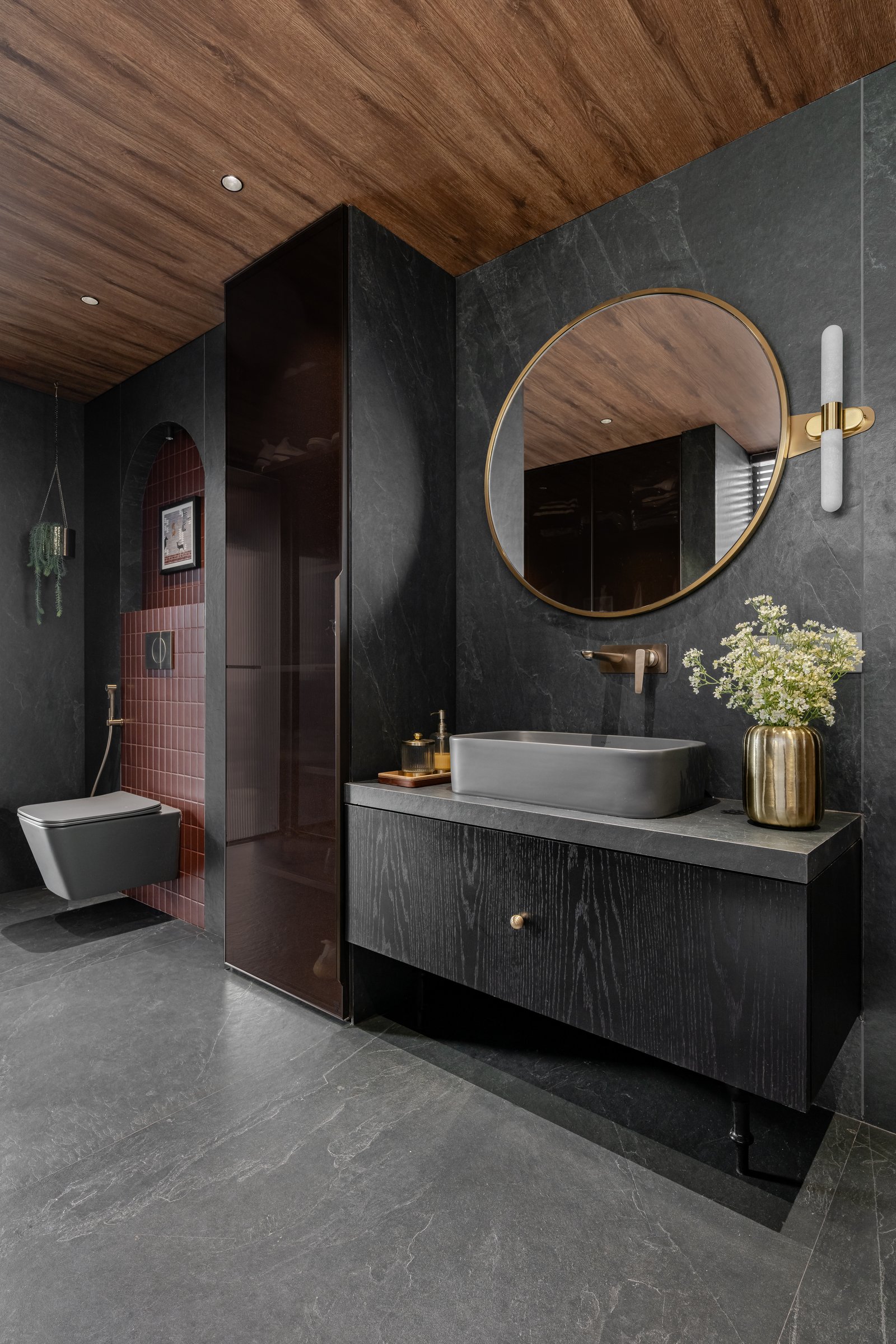 A bathroom with dark stone walls, timber ceiling, and a terracotta-tiled arched alcove that introduces unexpected colour
