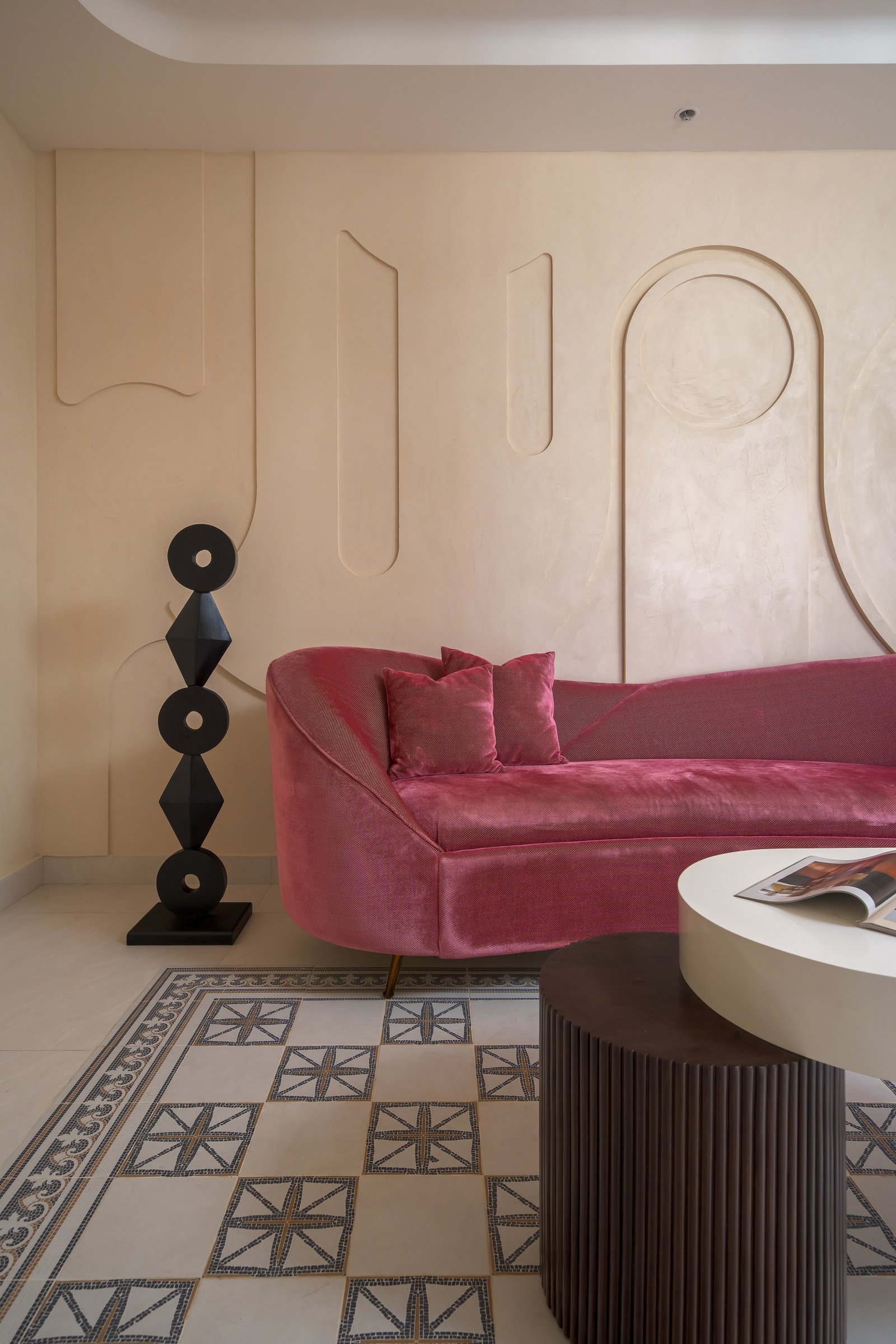 A maroon velvet curved sofa against the living room's incised plaster wall, with mosaic floor tiles grounding the composition