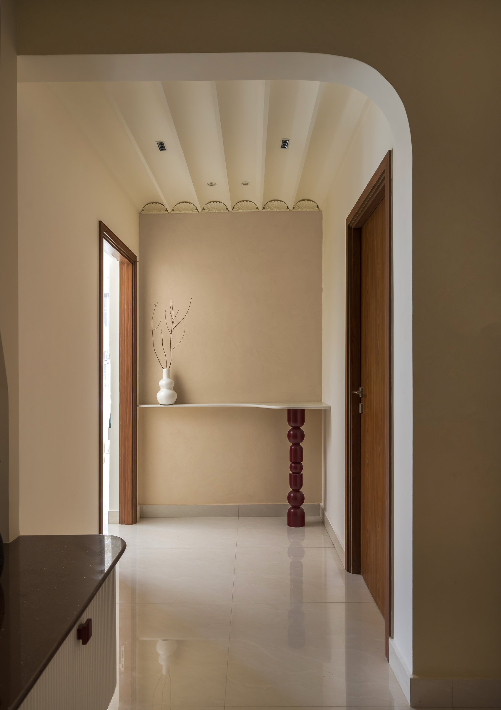 A passage between zones, where a scalloped ceiling detail and a sculptural console table sustain the design language