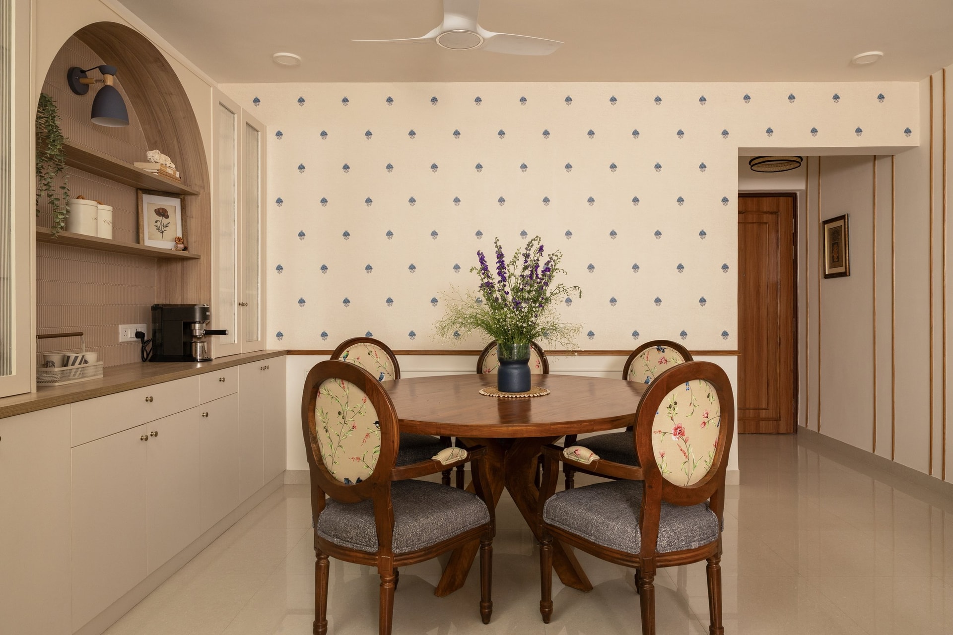 The dining area wrapped in the same blue-motif wallpaper, with an arched niche lending soft geometry to the storage wall