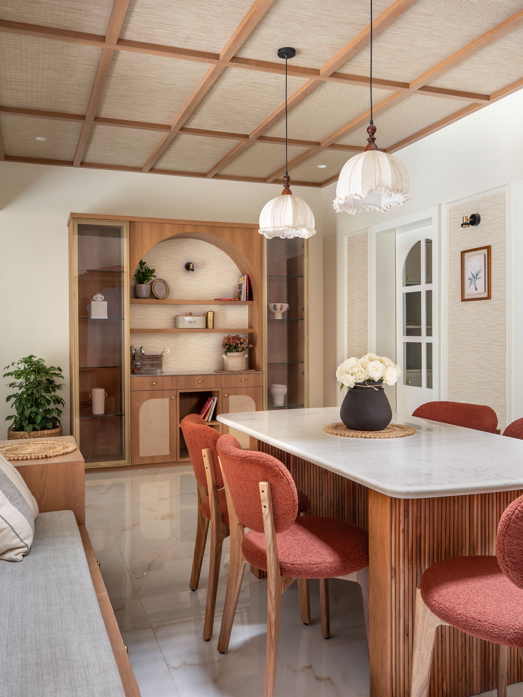 The dining area beneath a cane-and-wood coffered ceiling, terracotta bouclé chairs warming the marble table