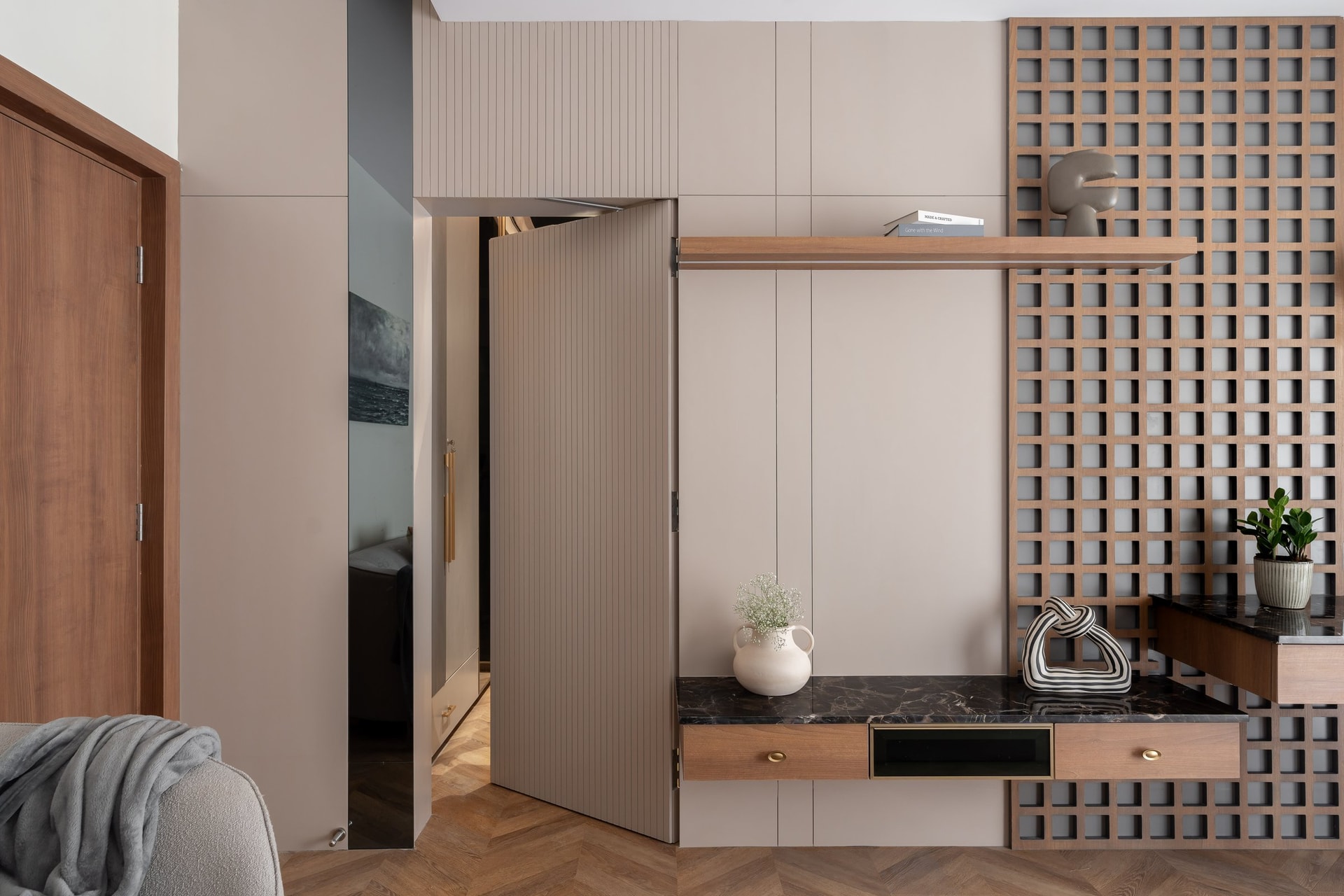 A reeded pivoting door opens onto a lattice-wrapped console in the bedroom passage