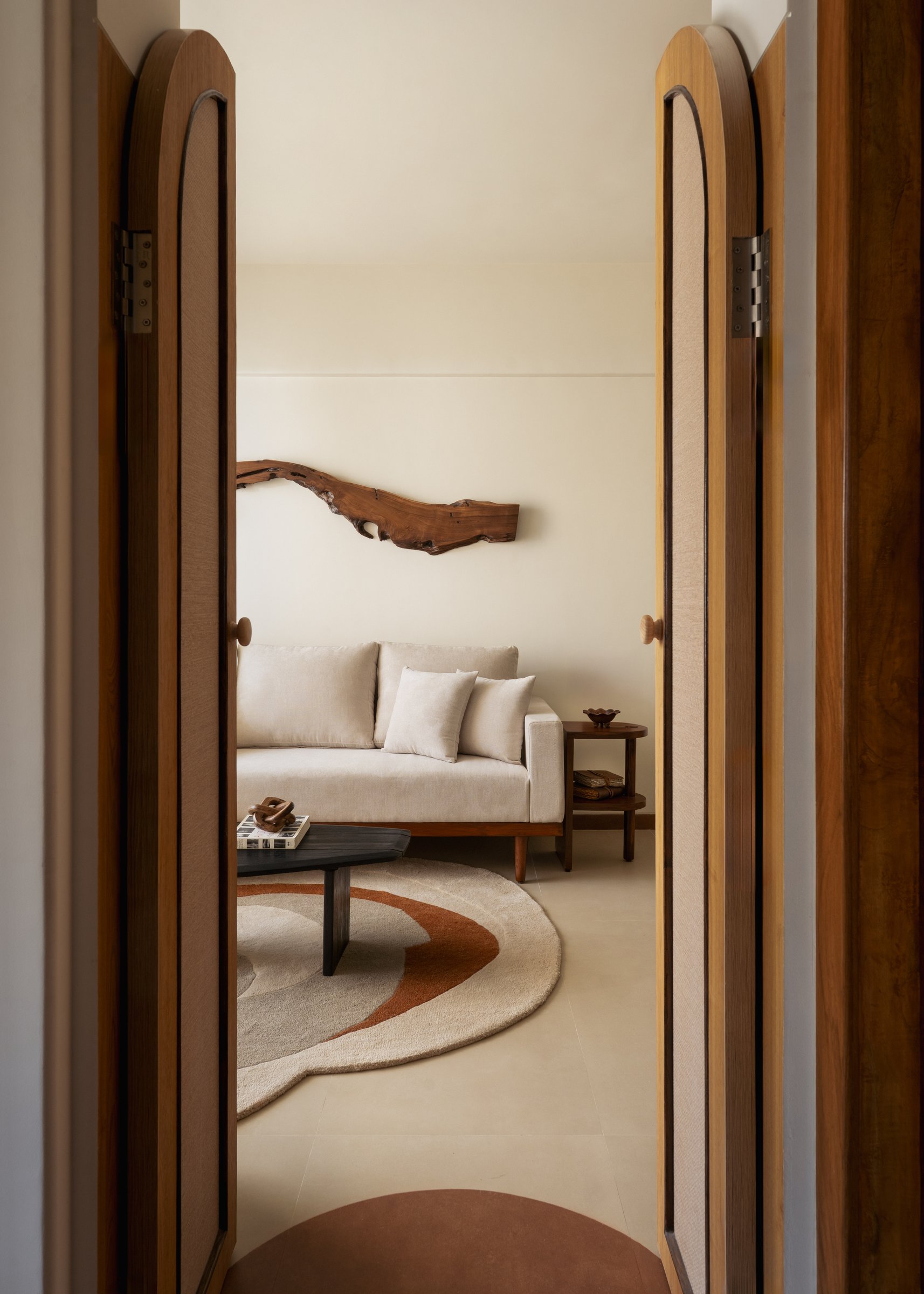 Glimpsed through arched cane doors, the master bedroom continues the driftwood-and-terracotta vocabulary