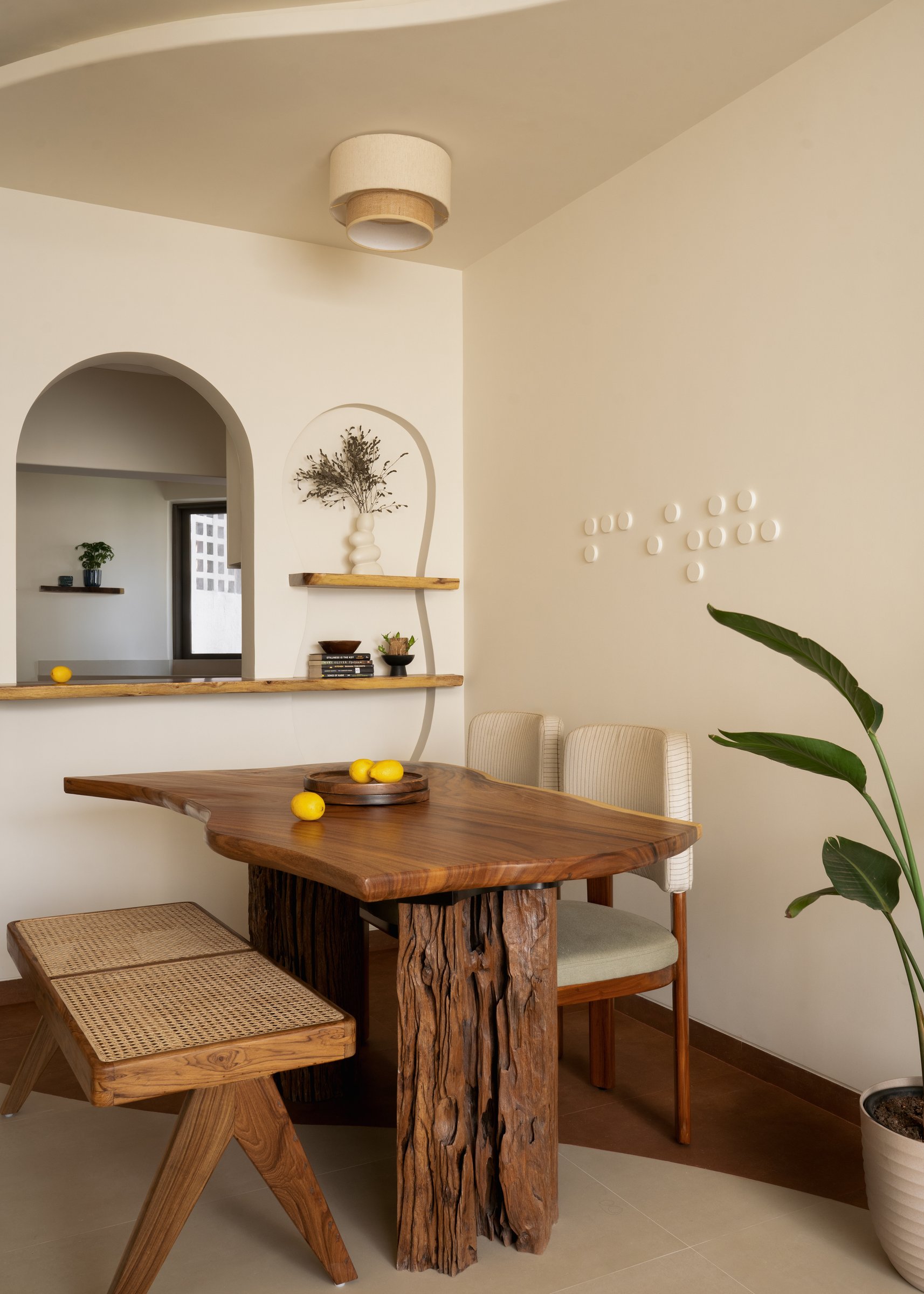 A Jeanneret-language cane bench, an internal window to the kitchen, and layered arches behind