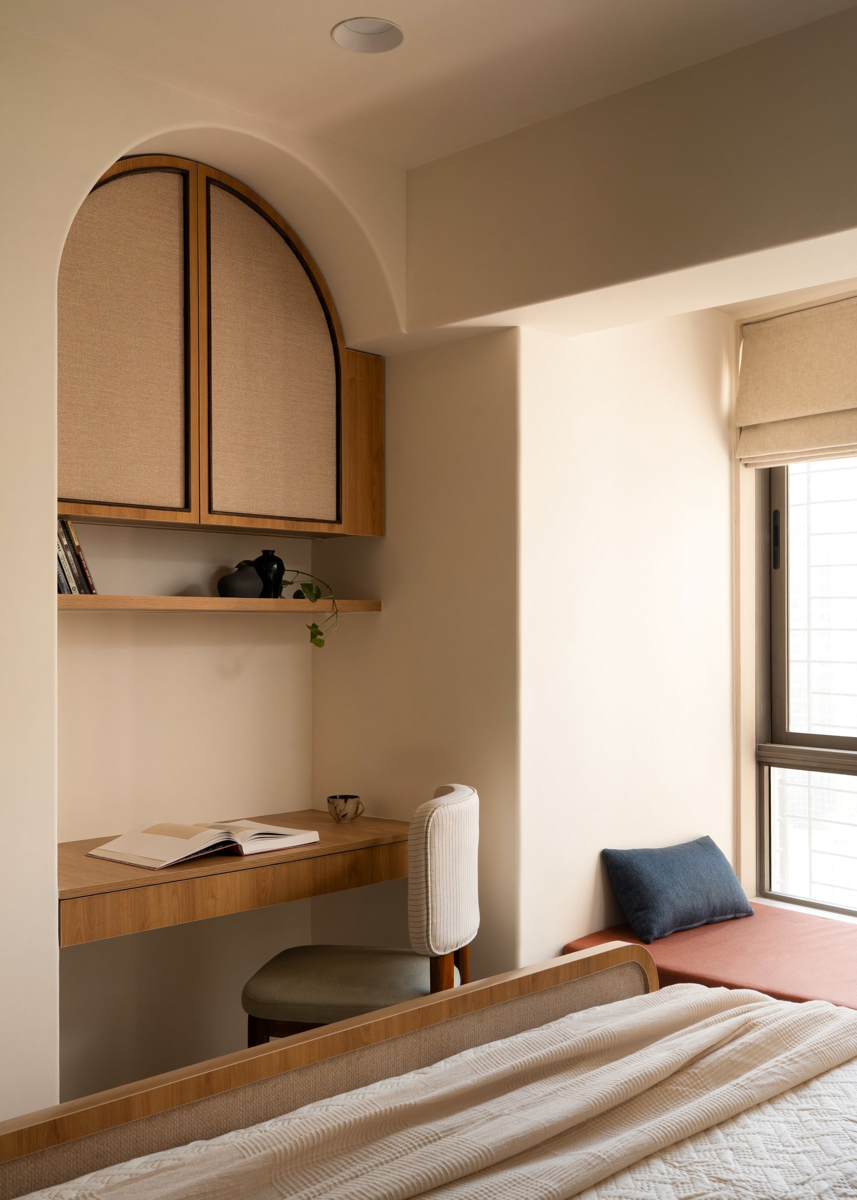 A writing alcove crowned by an arched jute-faced cabinet, with a terracotta-linen window seat alongside