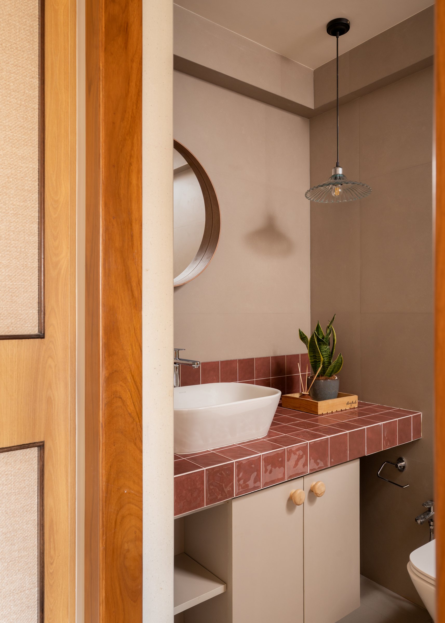 The master bath: oxblood tile, a circular timber-framed mirror, and a fluted glass pendant