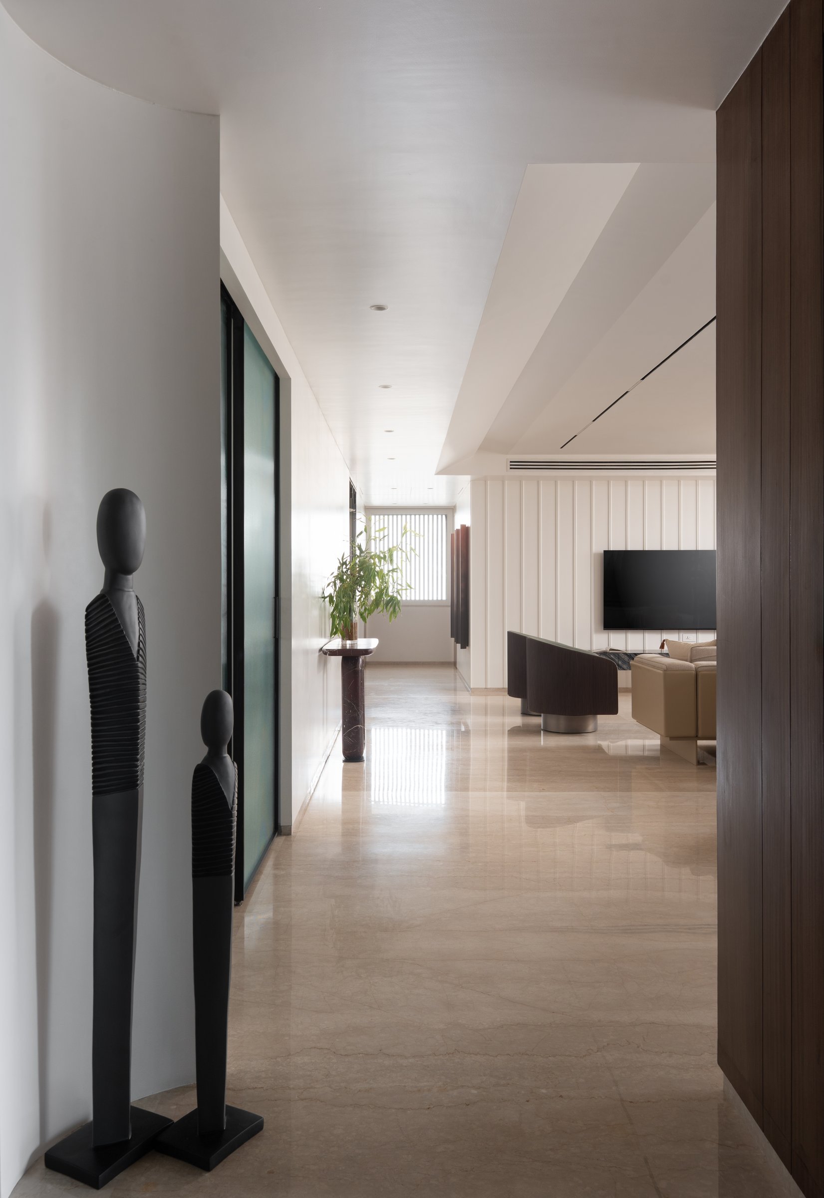The entry passage in honed stone, where two slender figurative sculptures perform the role a foyer might have played
