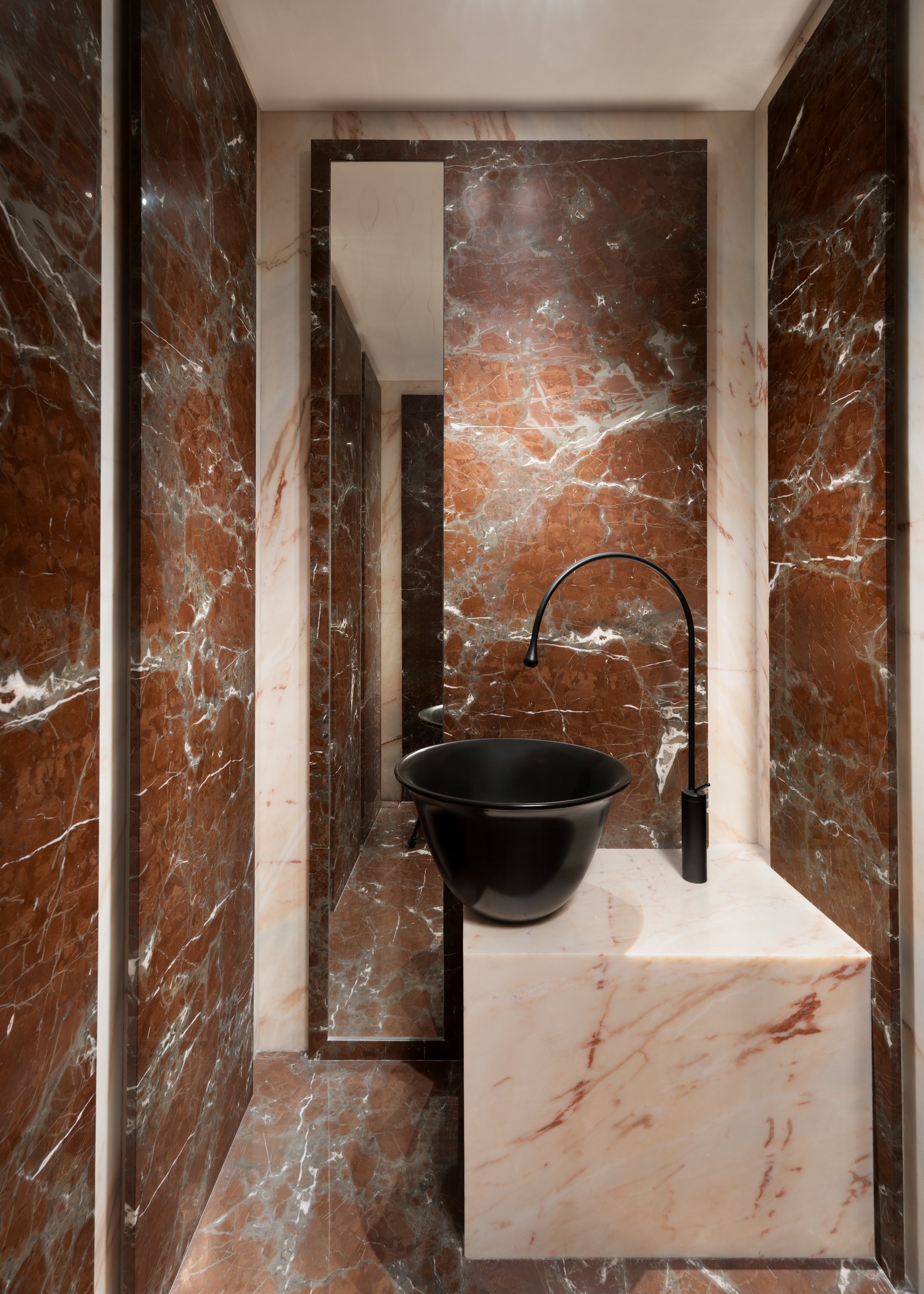 The guest powder room: rojo marble walls, a pale onyx vanity, and a matte black basin that reads as sculpture