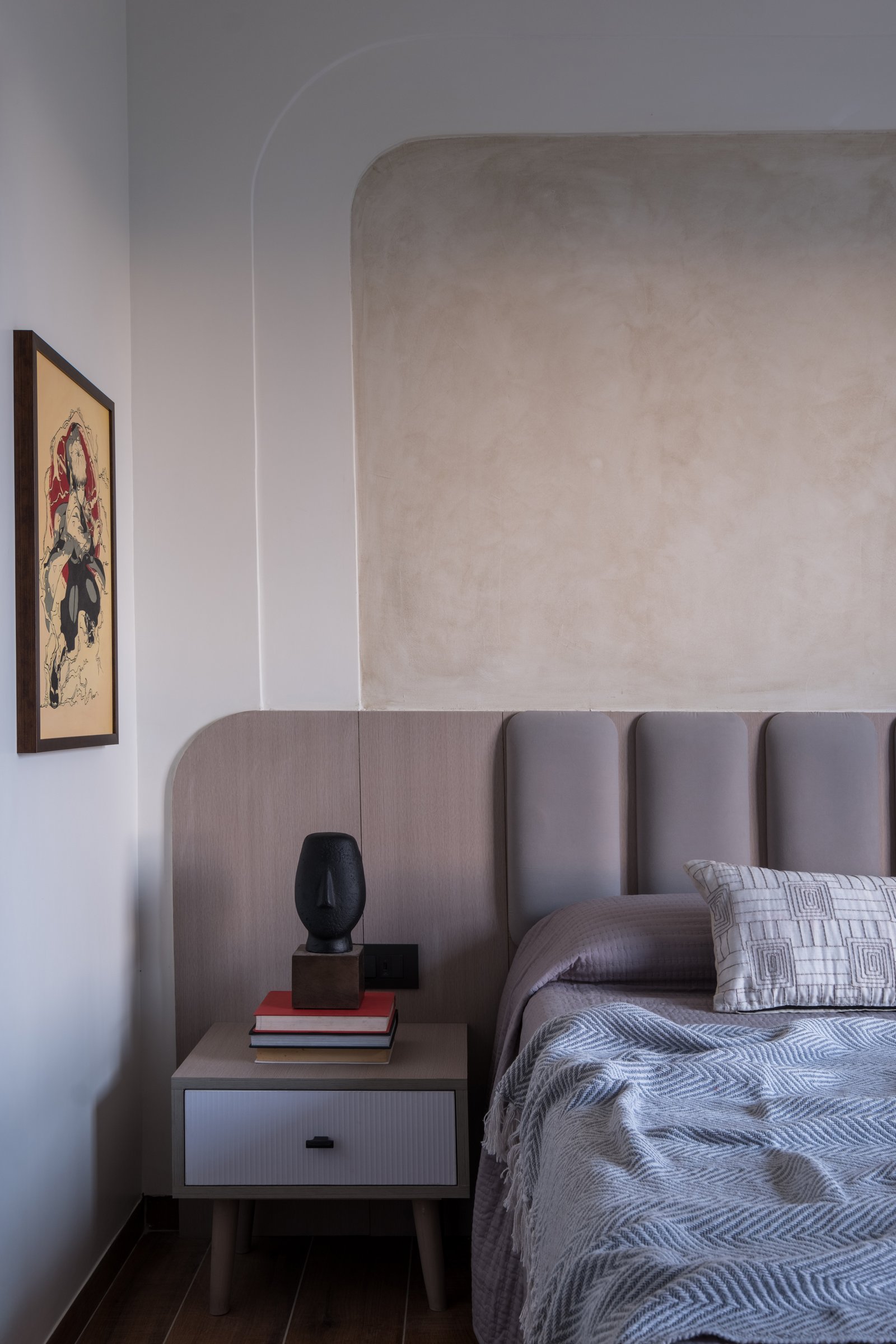 The bedside detail, where a sculpted black face vessel sits above a stack of books