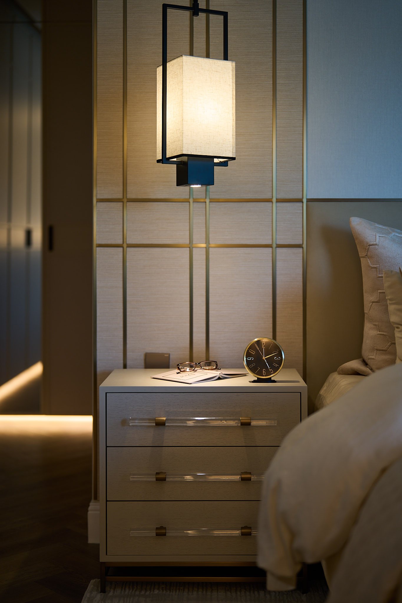 The bedside detail, where acrylic-and-brass pulls and a linen lantern domesticate hotel-grade craft