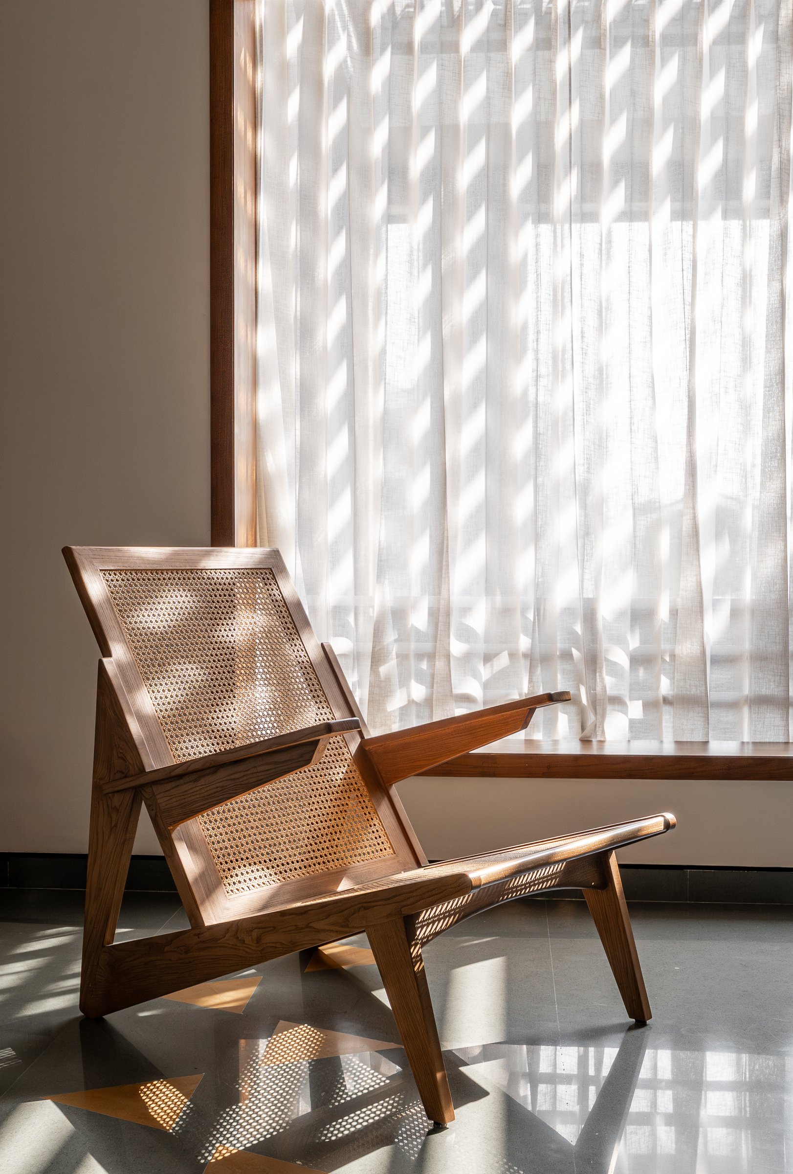 A cane lounge chair in the library, lit by diagonal shadows cast through the exterior jaali screen