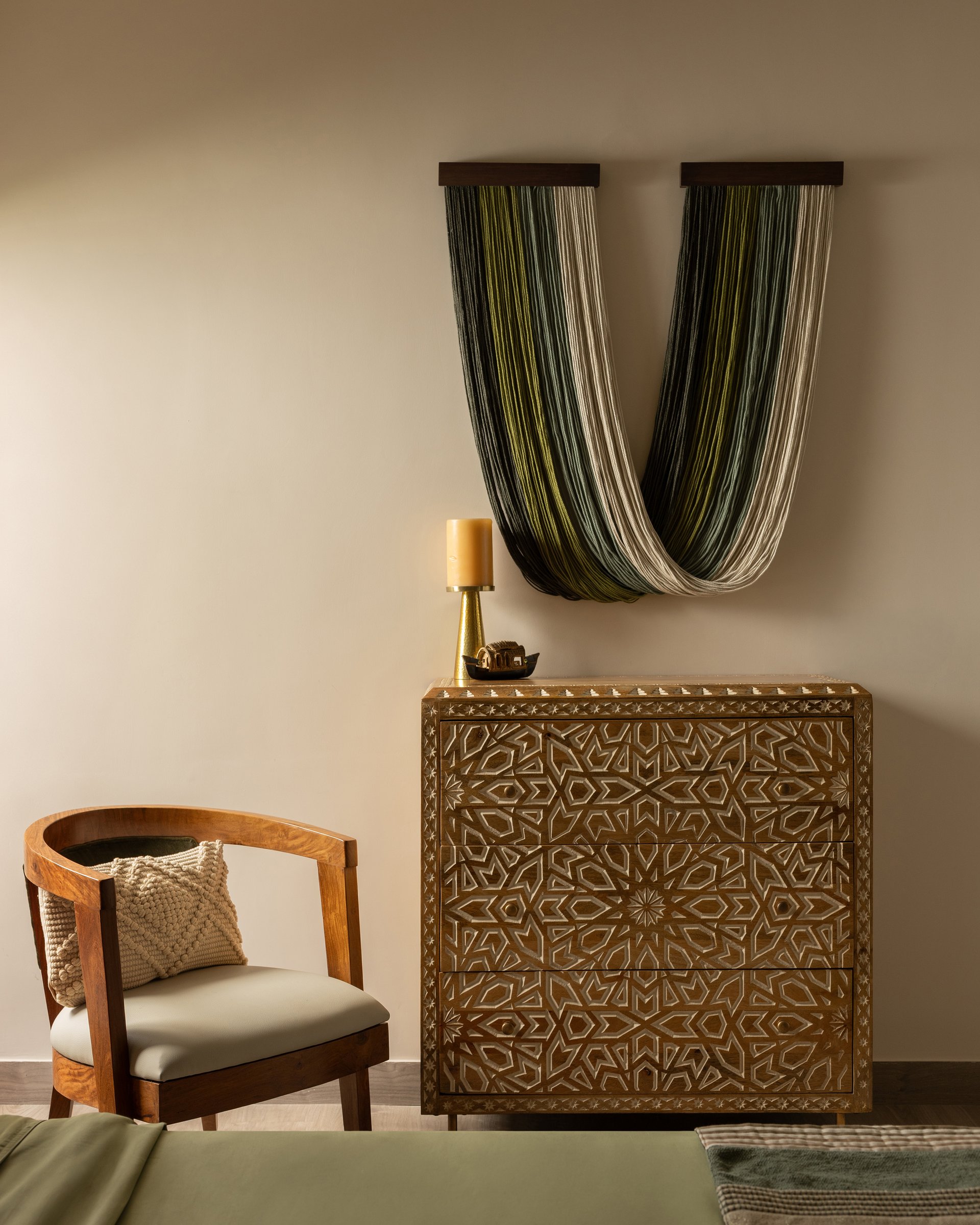 A carved timber chest and draped fibre wall installation form the bedroom's most craft-forward corner