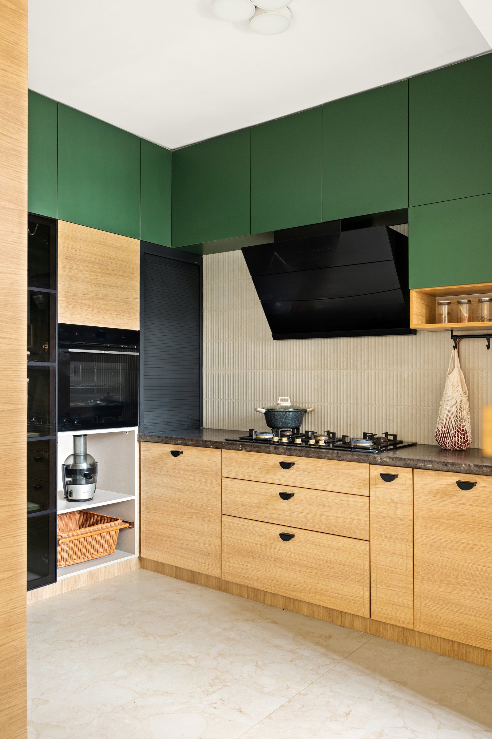 The working kitchen drops the floral lightness for forest green and pale timber, calmly anchored