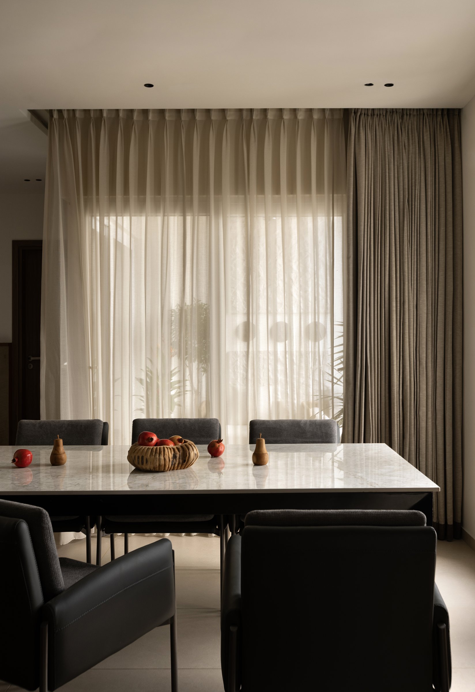 Layered sheer and taupe curtains filter Chennai's afternoon light onto a marble tabletop