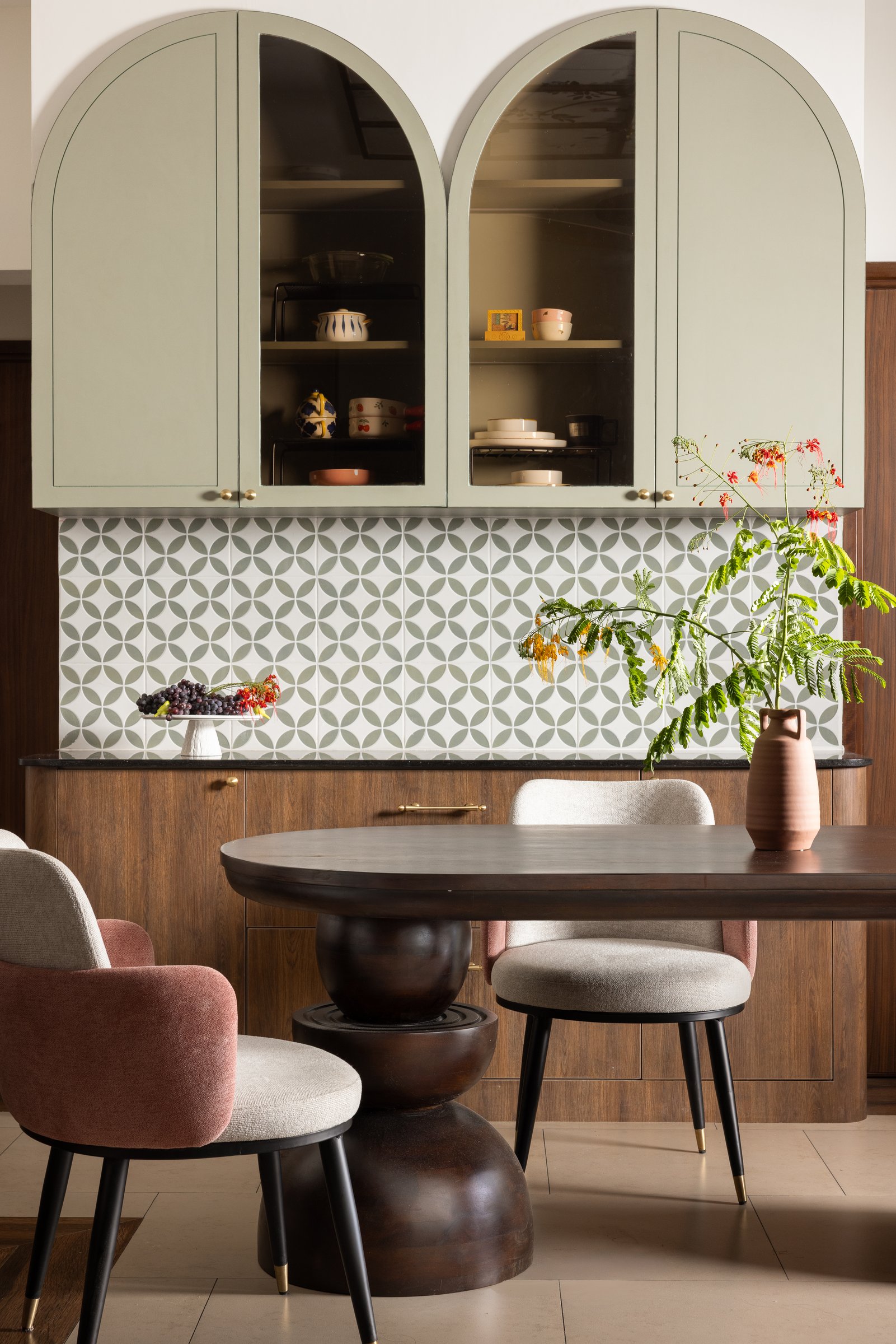 Twin arched sage cabinets above a geometric tiled backsplash anchor the dining area, with the family's commissioned hardwood table at its centre