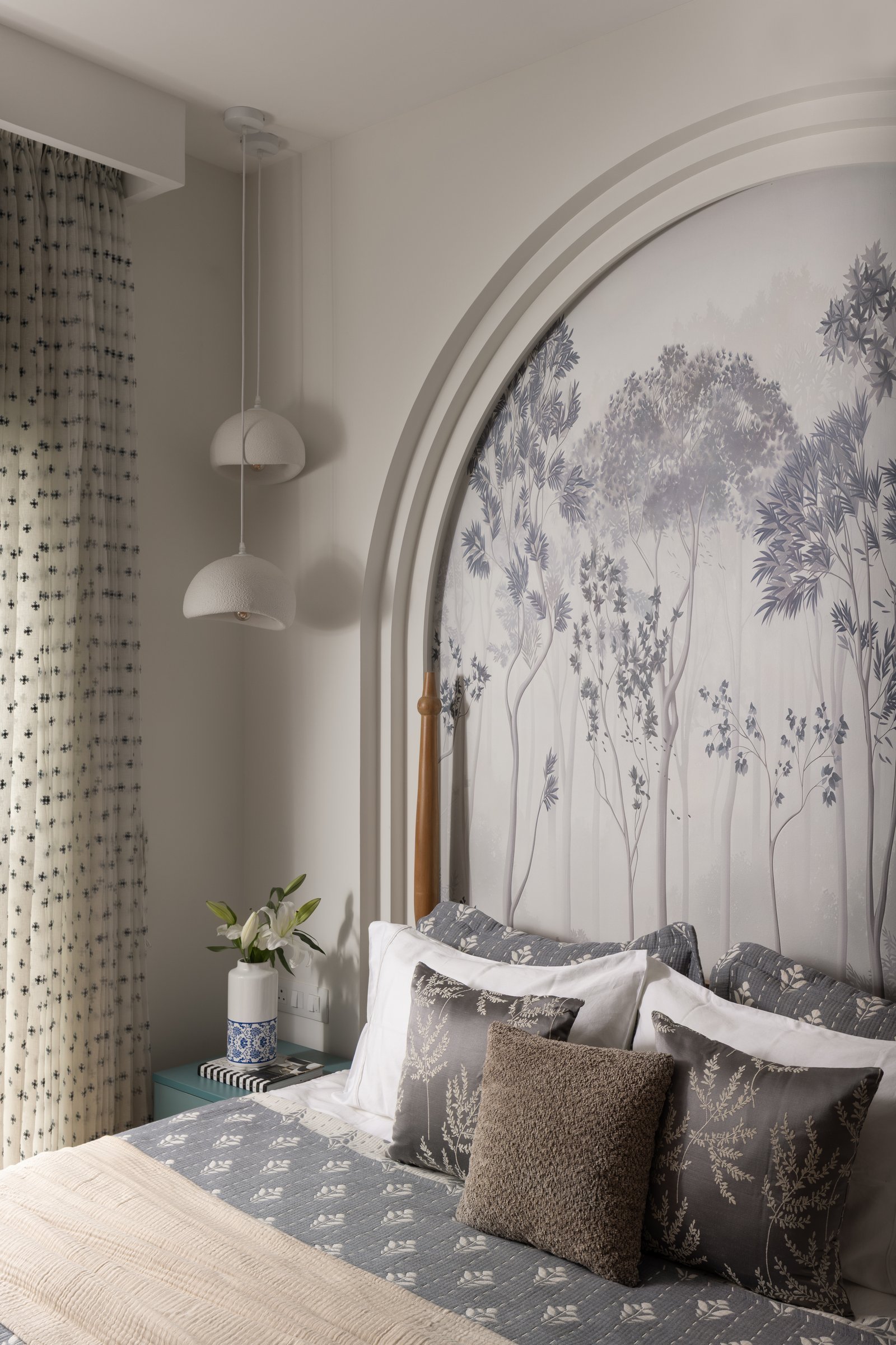 In the parents' bedroom, a grey-toned forest mural fills a deep arched recess, balanced by textured plaster pendants on long cords