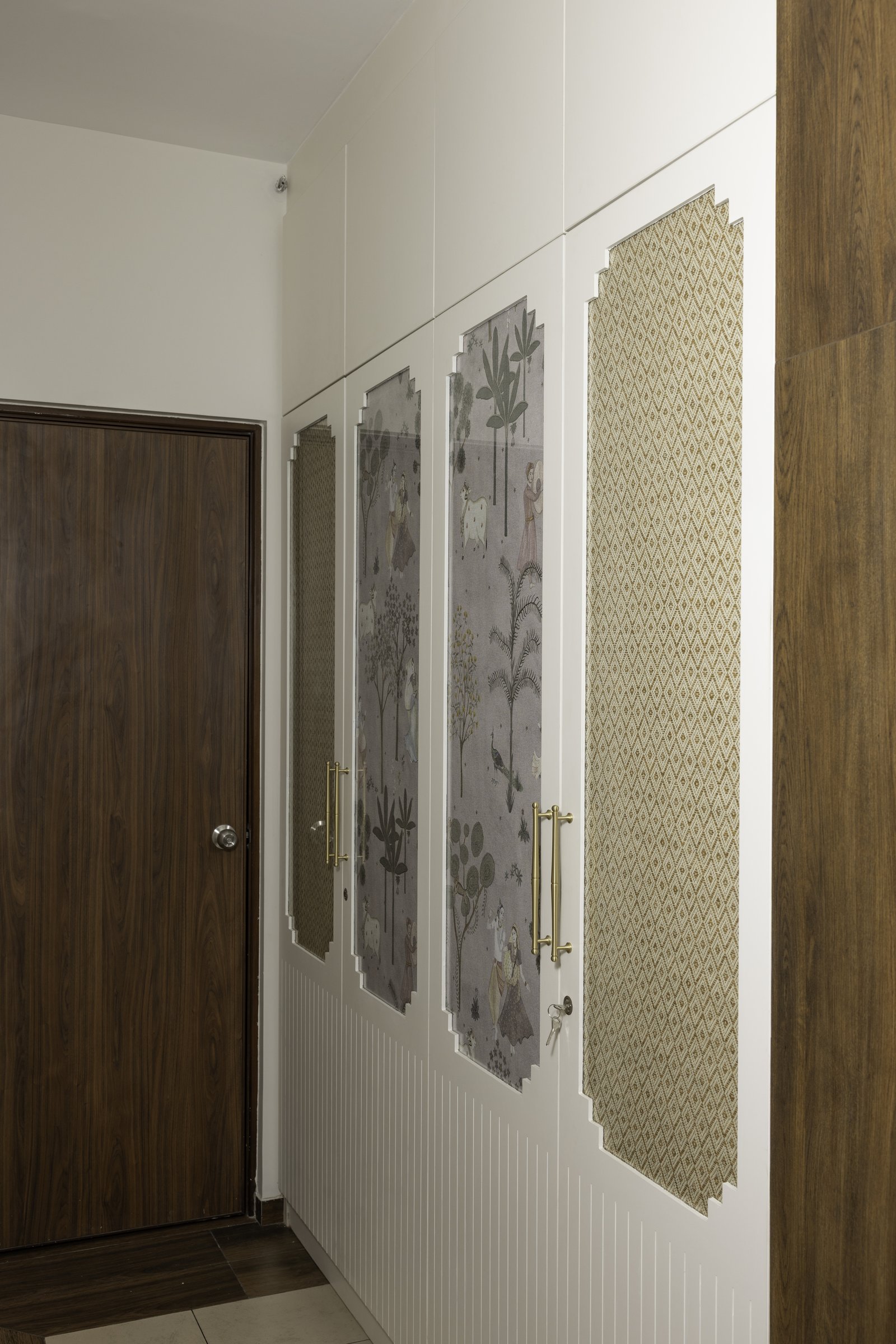 Pichwai-inspired panels framed by stepped white architraves turn entry storage into a quiet exhibition of heritage motifs