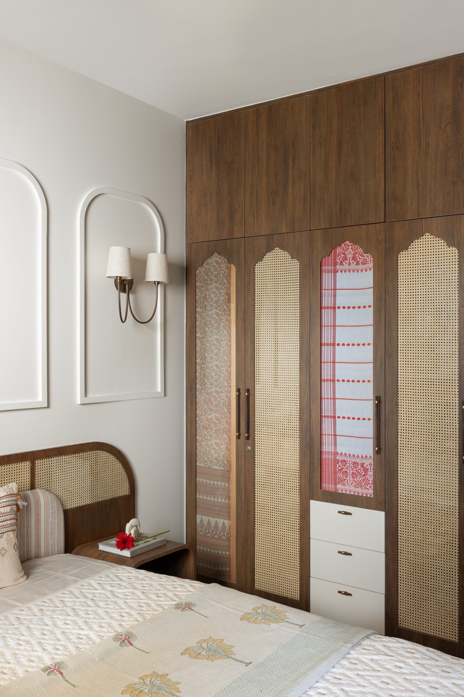 Heritage textiles gifted by the couple's in-laws, set behind cane and glass within the wardrobe fronts: structural memory, made domestic