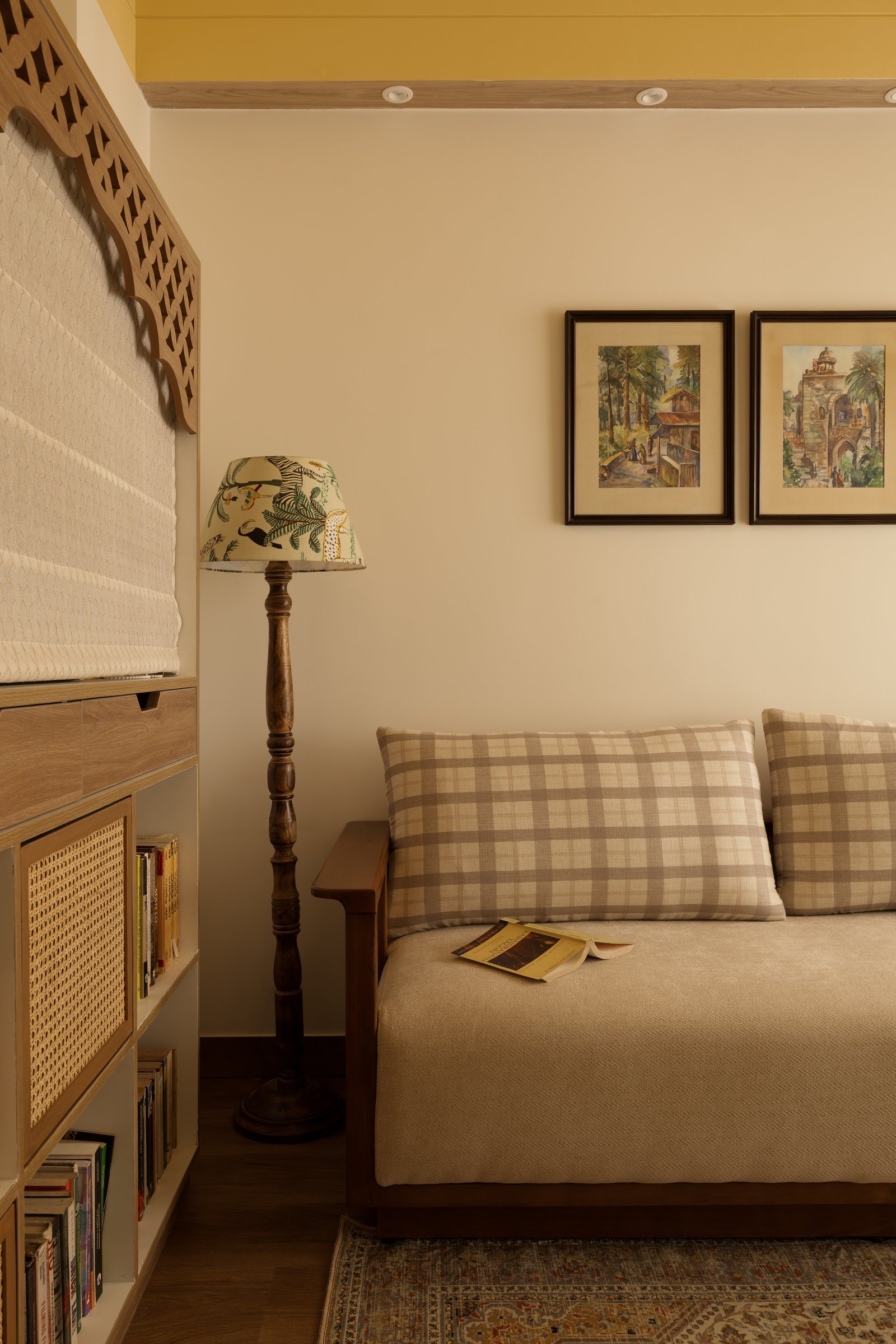 A daybed corner within the study, where cane-fronted shelving and watercolour landscapes invite slow reading