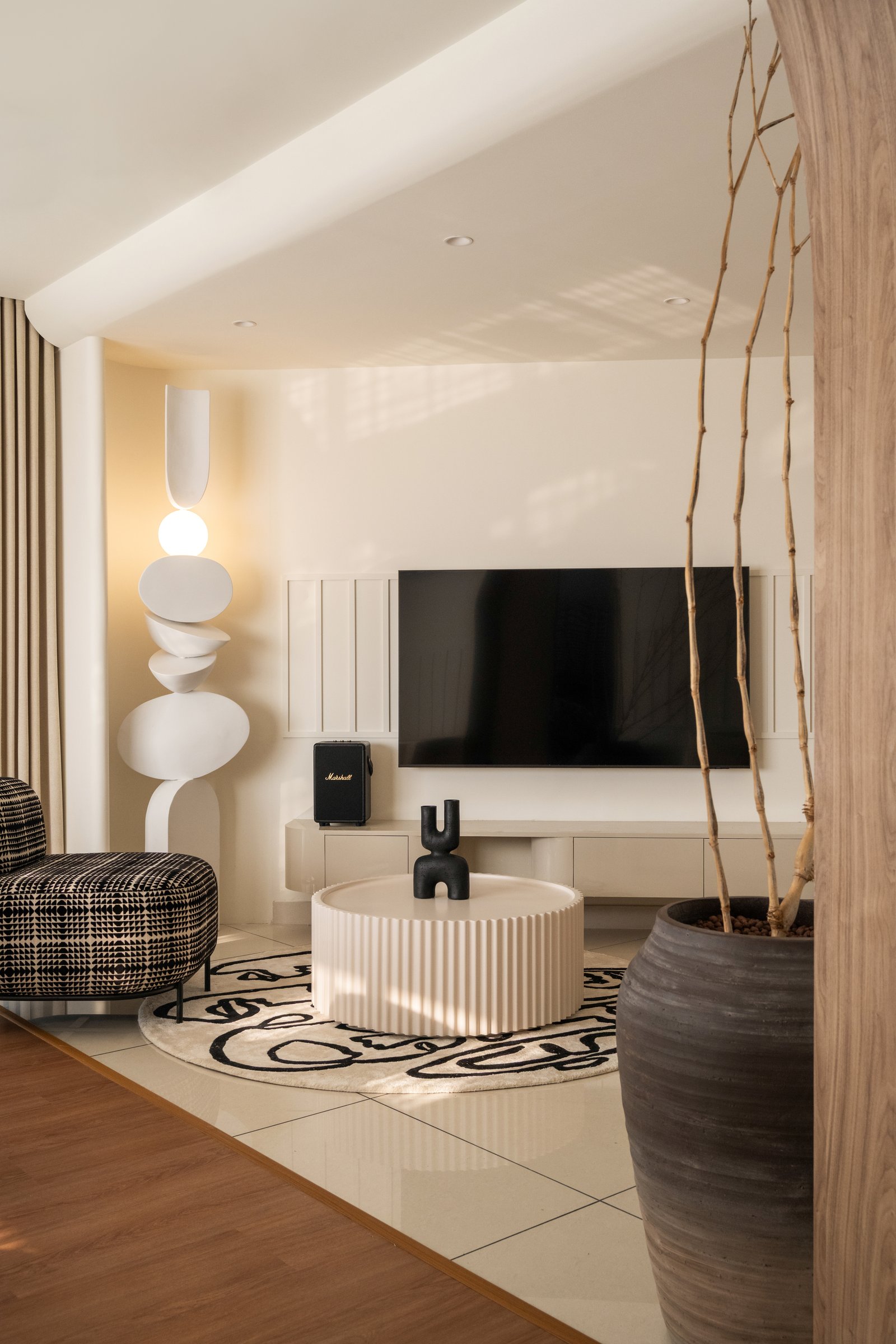 The living room sets the tonal argument of the home: fluted cream coffee table, sculptural stacked-form floor lamp, and a patterned lounge chair as graphic counterpoint