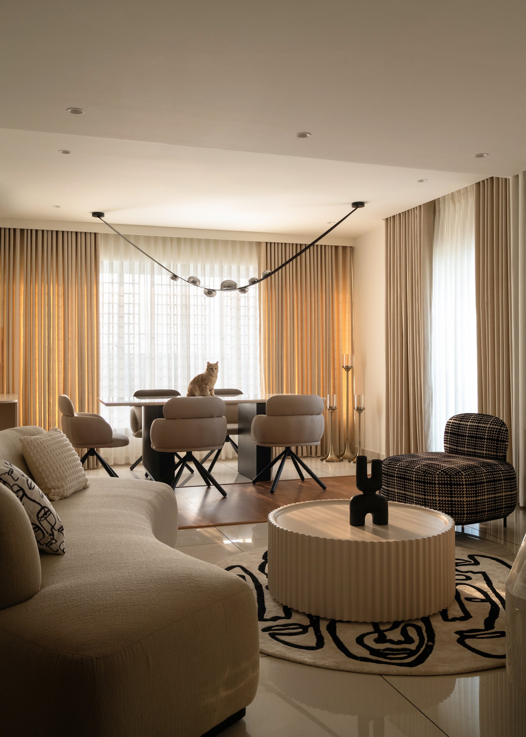Seen wider: a curved boucle sofa, a chrome-bead pendant strung like a drawn line, and the dining table held within a single volume