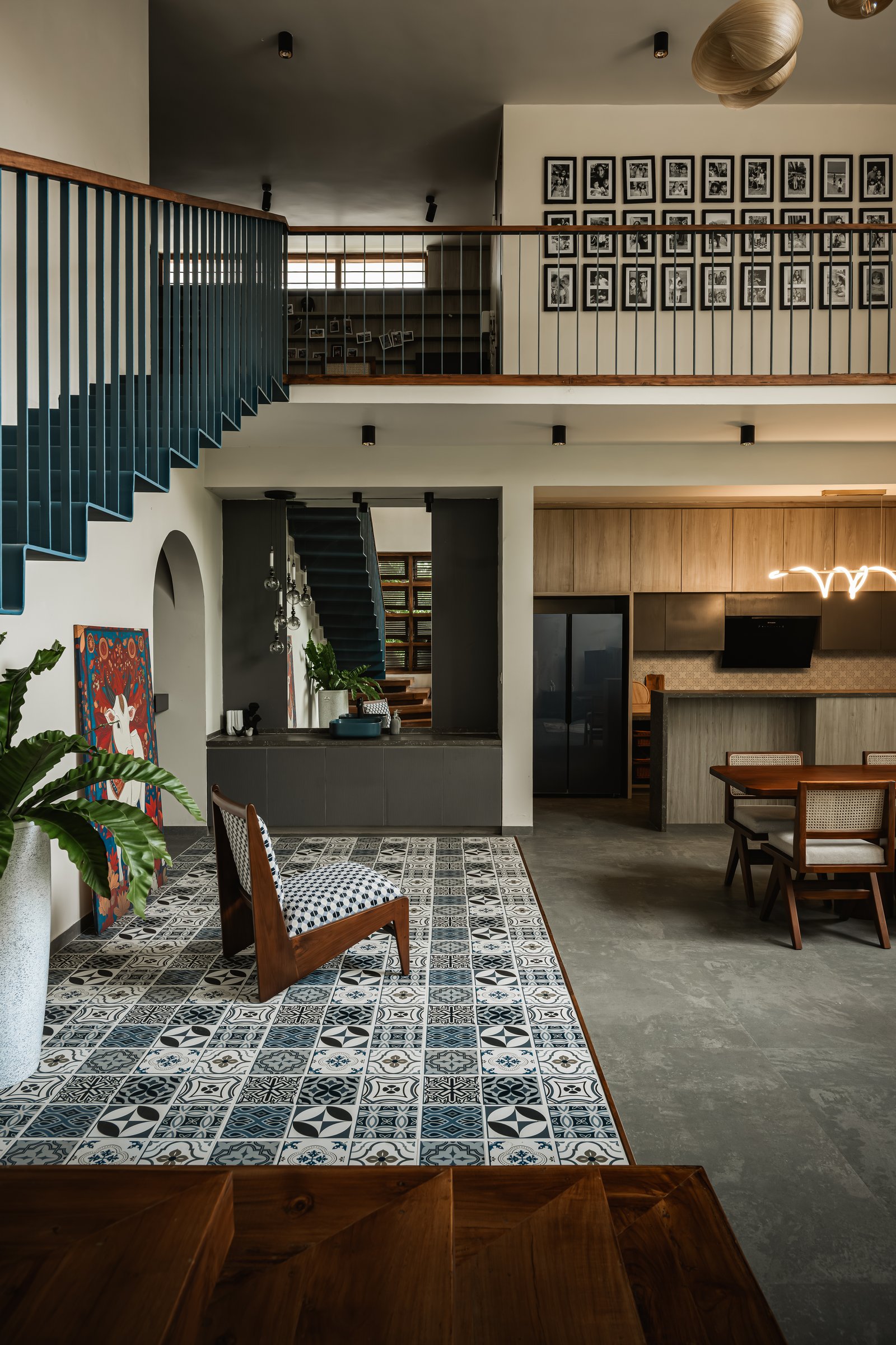 The double-height living volume, where a teal staircase and a mezzanine photo gallery hold the home's vertical drama in balance