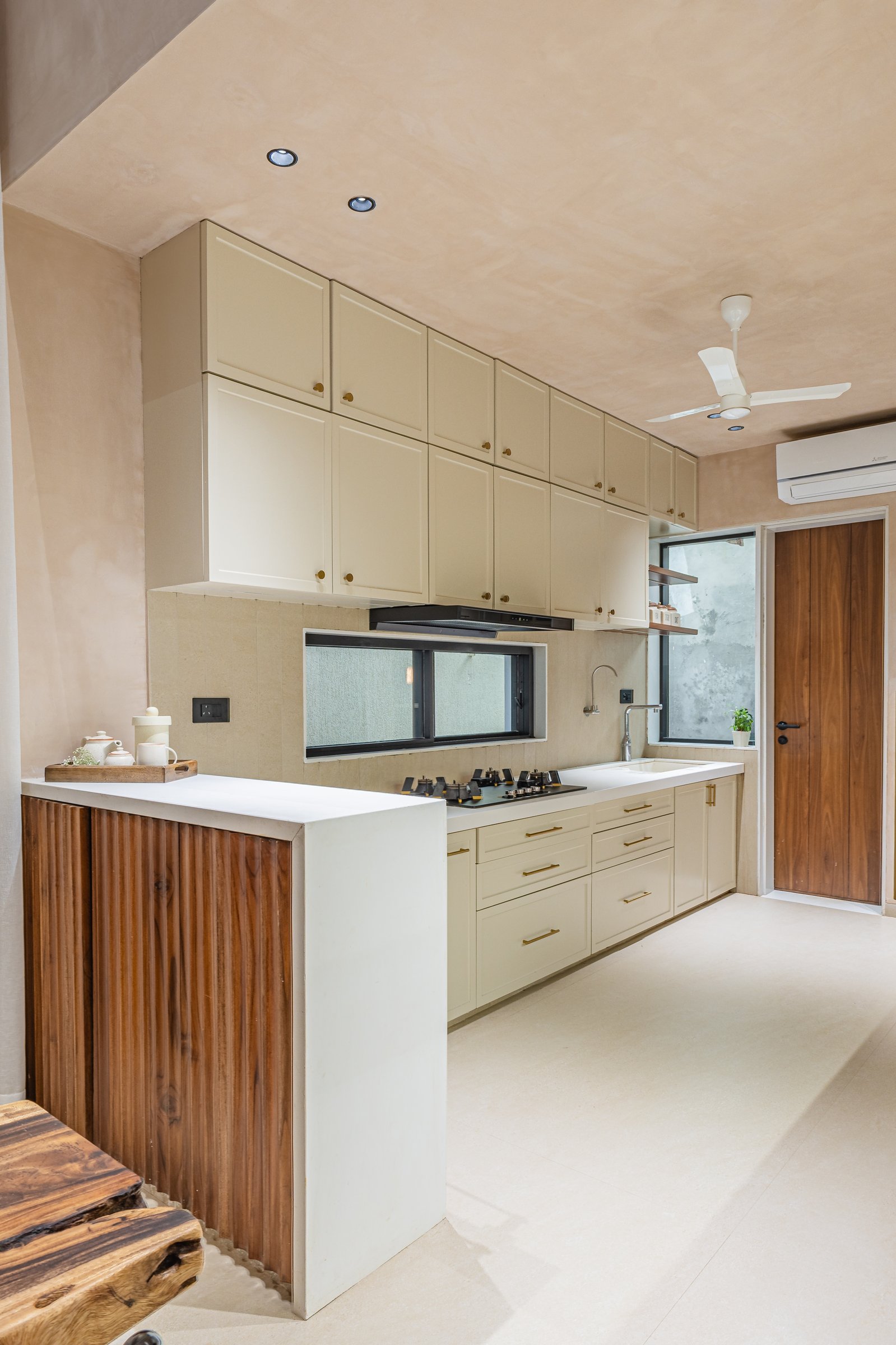 The kitchen takes a quieter line: cream cabinetry, brass pulls, and a fluted wood base on the peninsula