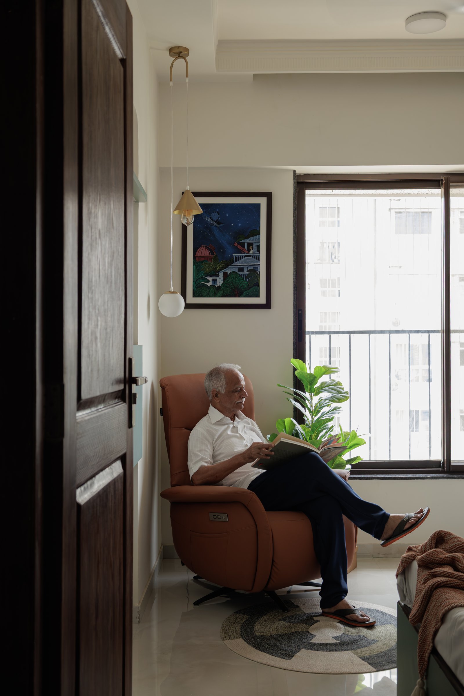 A reading corner in the master bedroom, with custom artwork by Yuga Desai and a tan recliner drawn close to the window