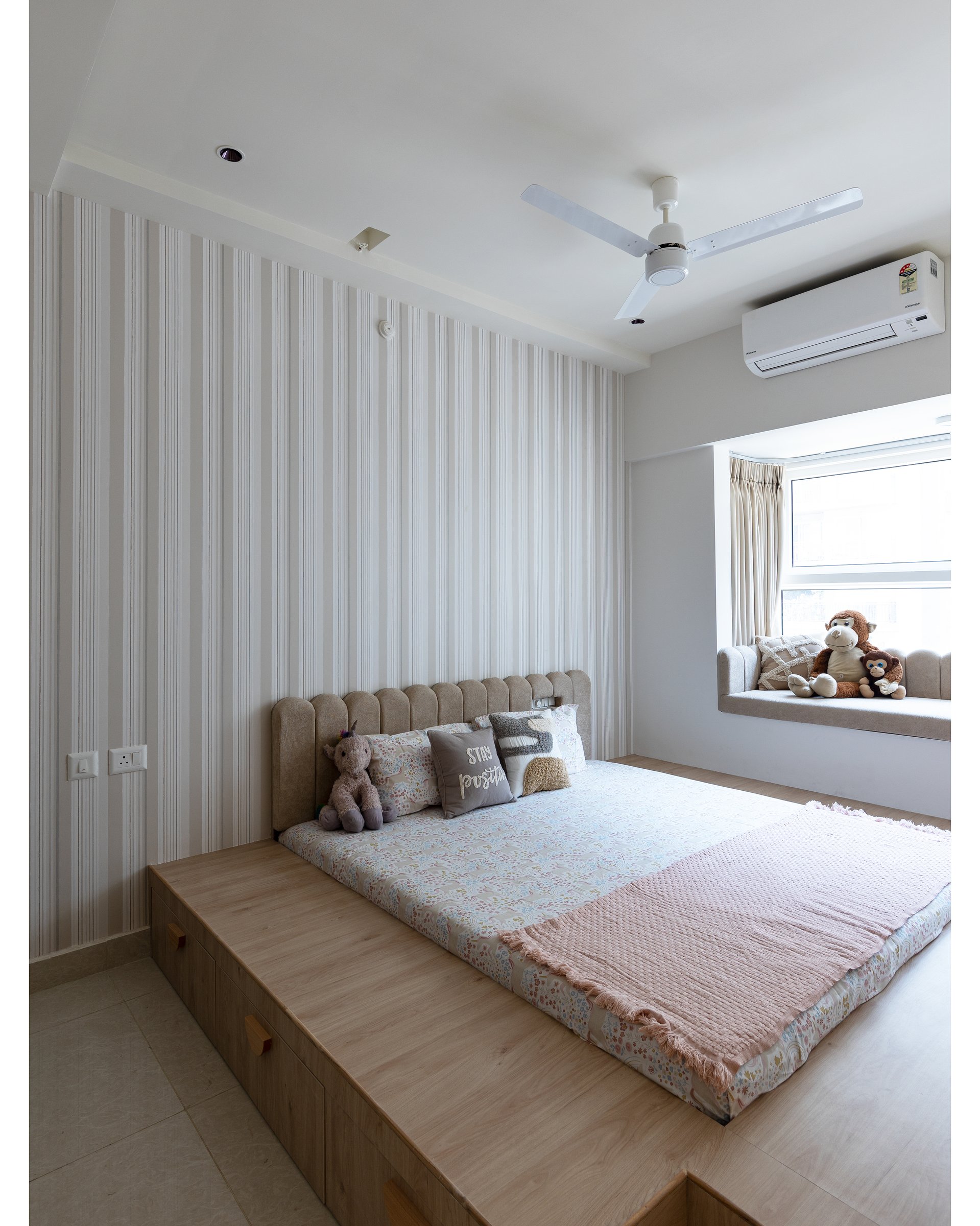 The children's bedroom, where a platform bed in blond hardwood meets a striped wallpapered wall and a generous window seat